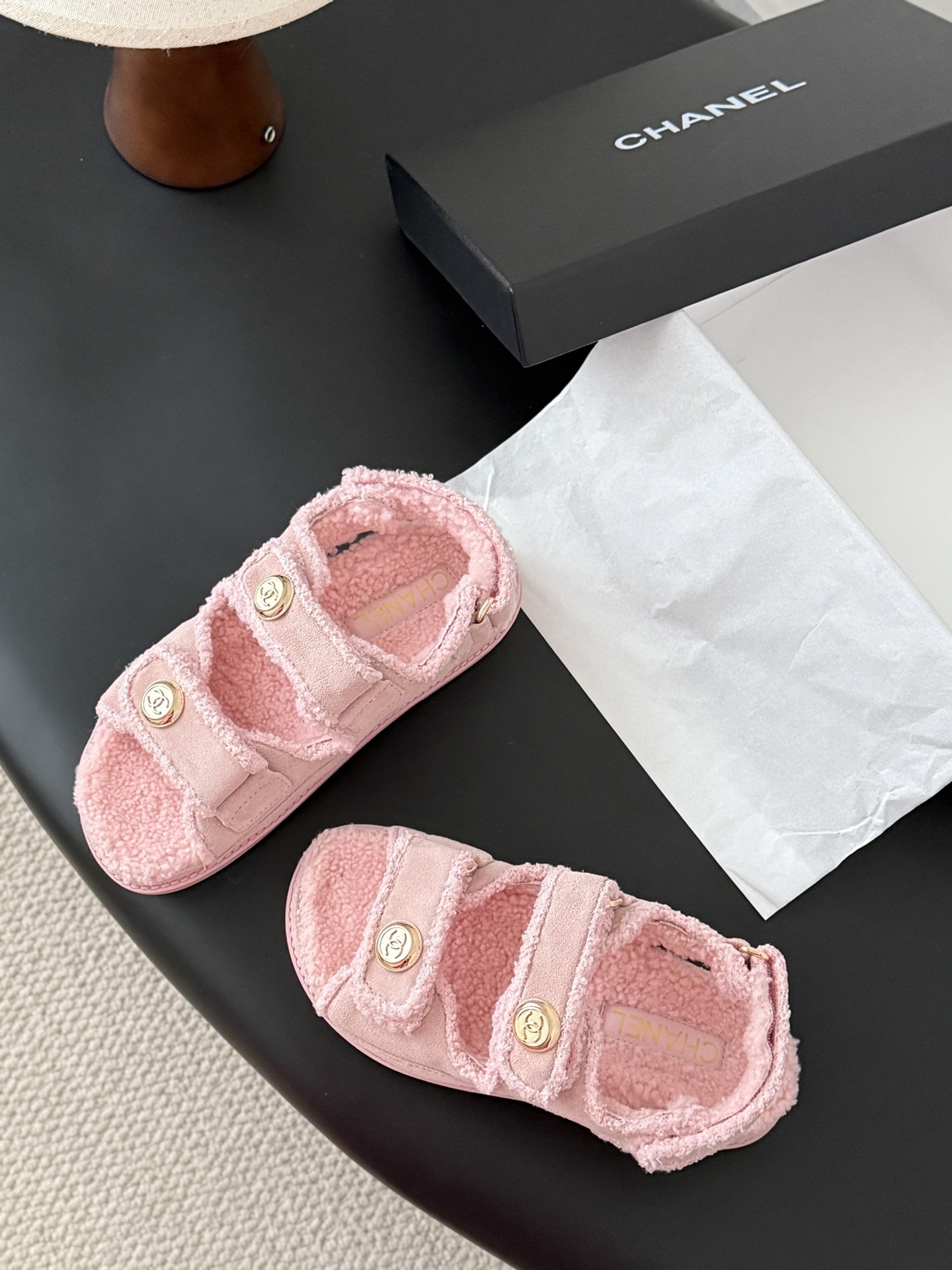 Pair of pink Chanel shearling sandals with gold CC logo buttons sitting next to a black Chanel box. - Hình 6