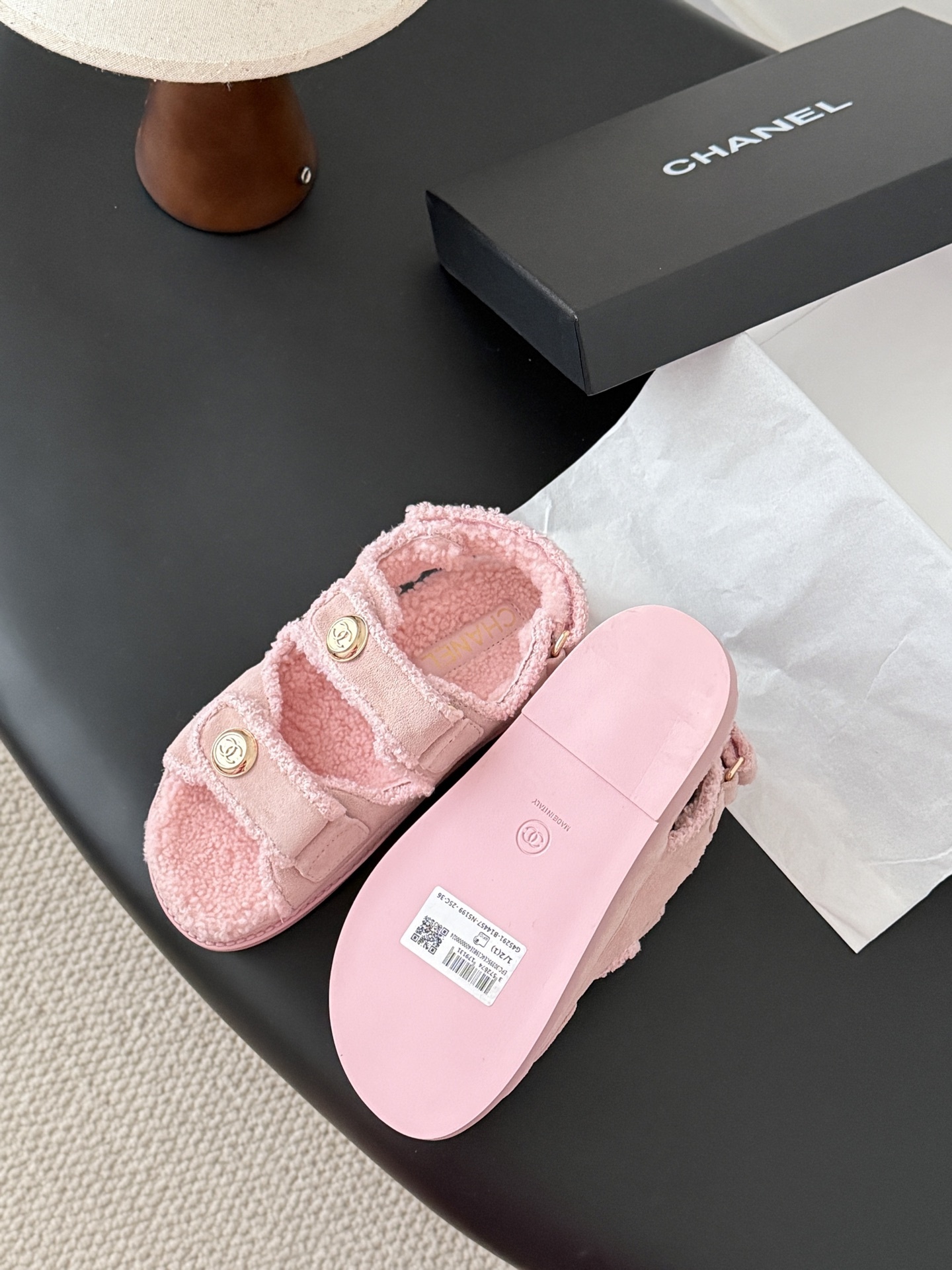 Pair of pink Chanel shearling sandals with gold CC logo buttons sitting next to a black Chanel box. - Hình 5