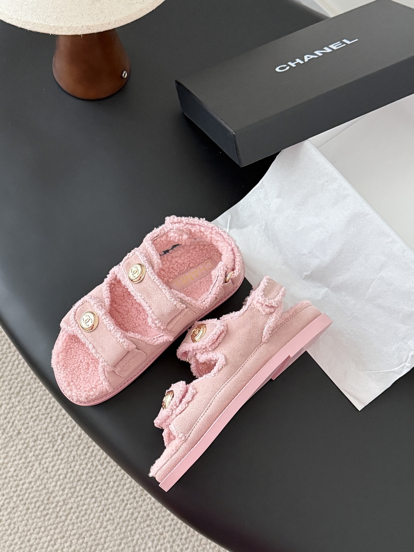 Pair of pink Chanel shearling sandals with gold CC logo buttons sitting next to a black Chanel box. - Hình 4