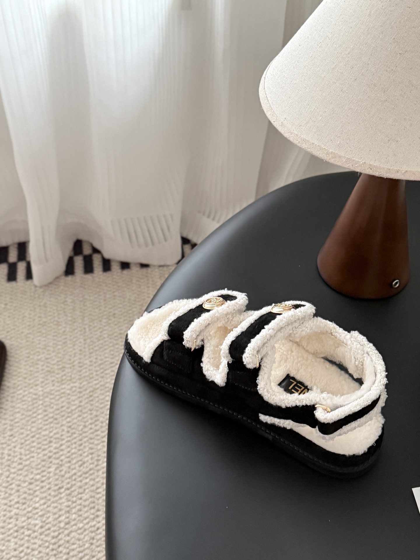 Chanel black and white shearling dad sandals with gold CC logo buttons on a black table next to a Chanel box - Hình 8