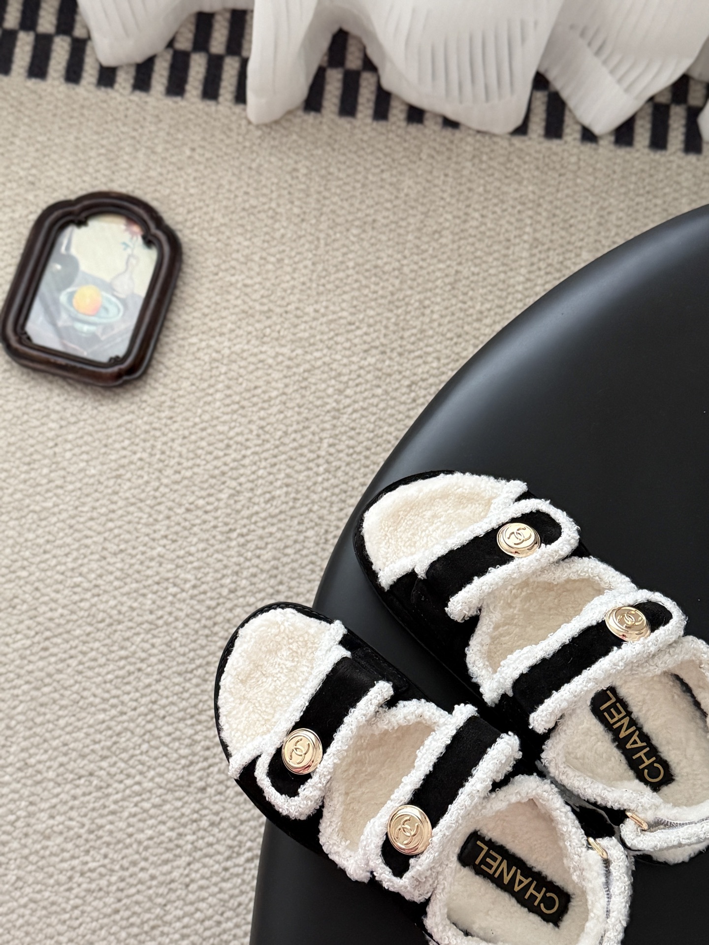 Chanel black and white shearling dad sandals with gold CC logo buttons on a black table next to a Chanel box - Hình 7