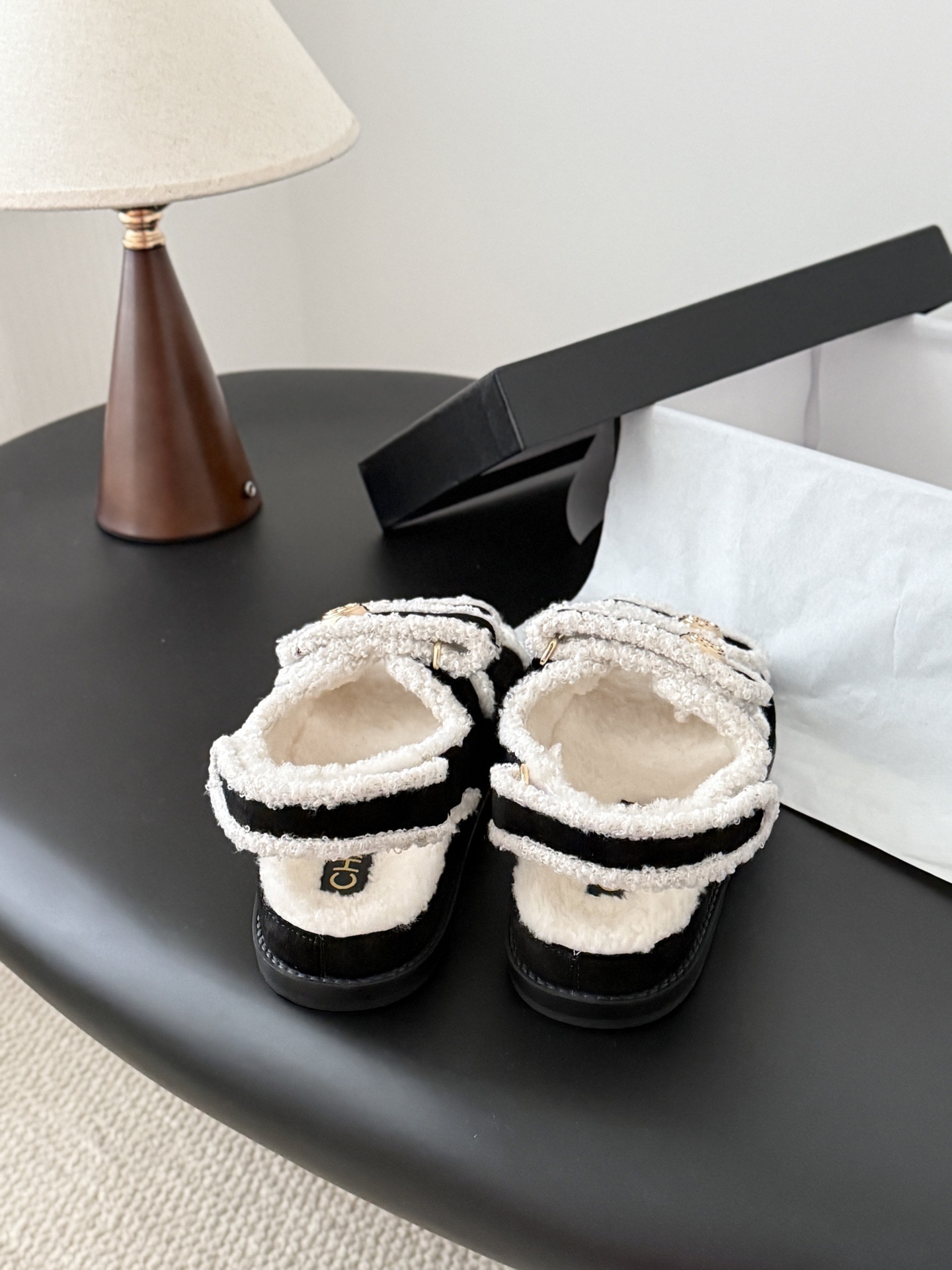 Chanel black and white shearling dad sandals with gold CC logo buttons on a black table next to a Chanel box - Hình 3