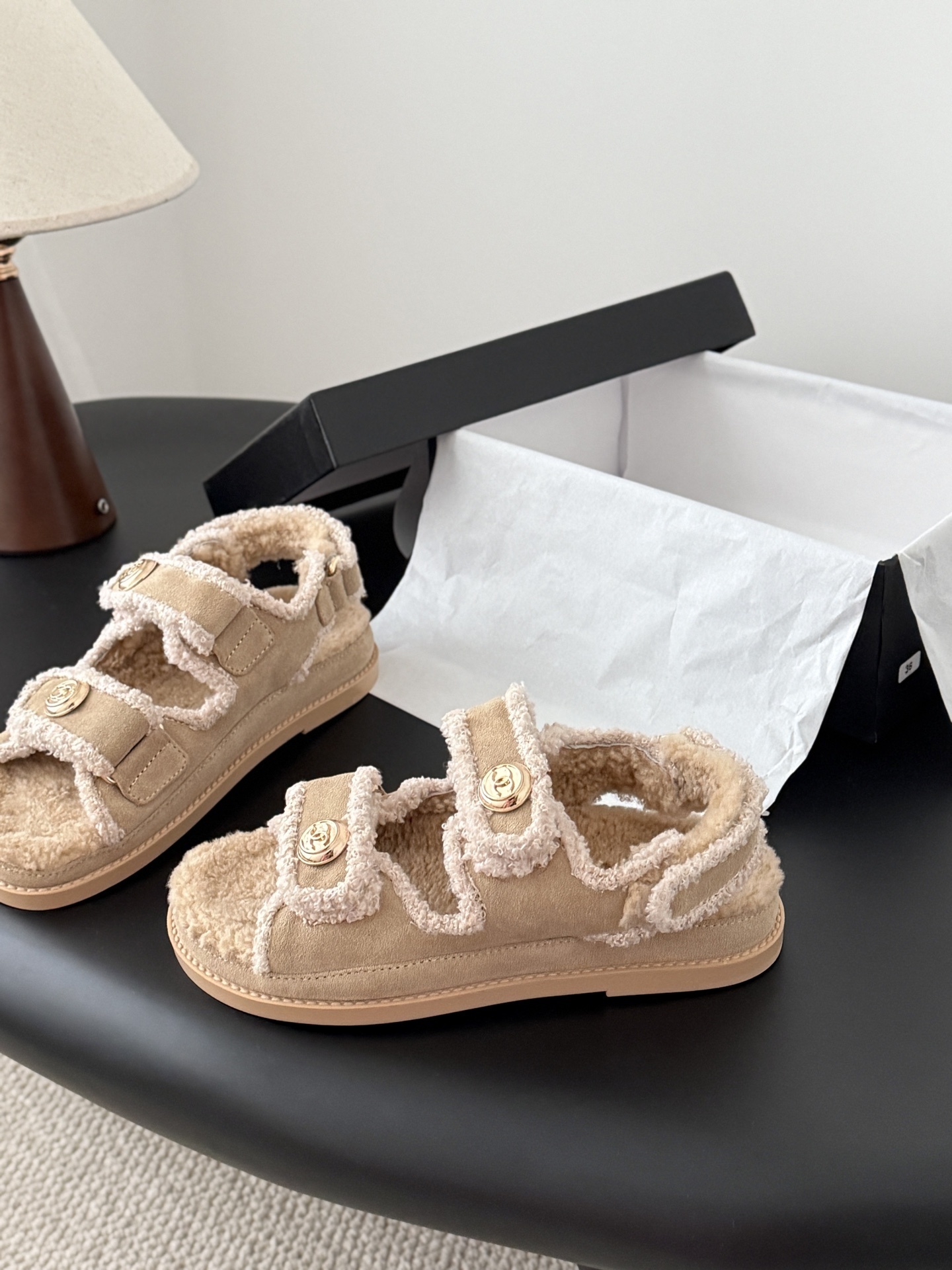 Luxury Chanel beige shearling dad sandals with gold CC logo buttons and fluffy lining placed next to a Chanel box. - Hình 2