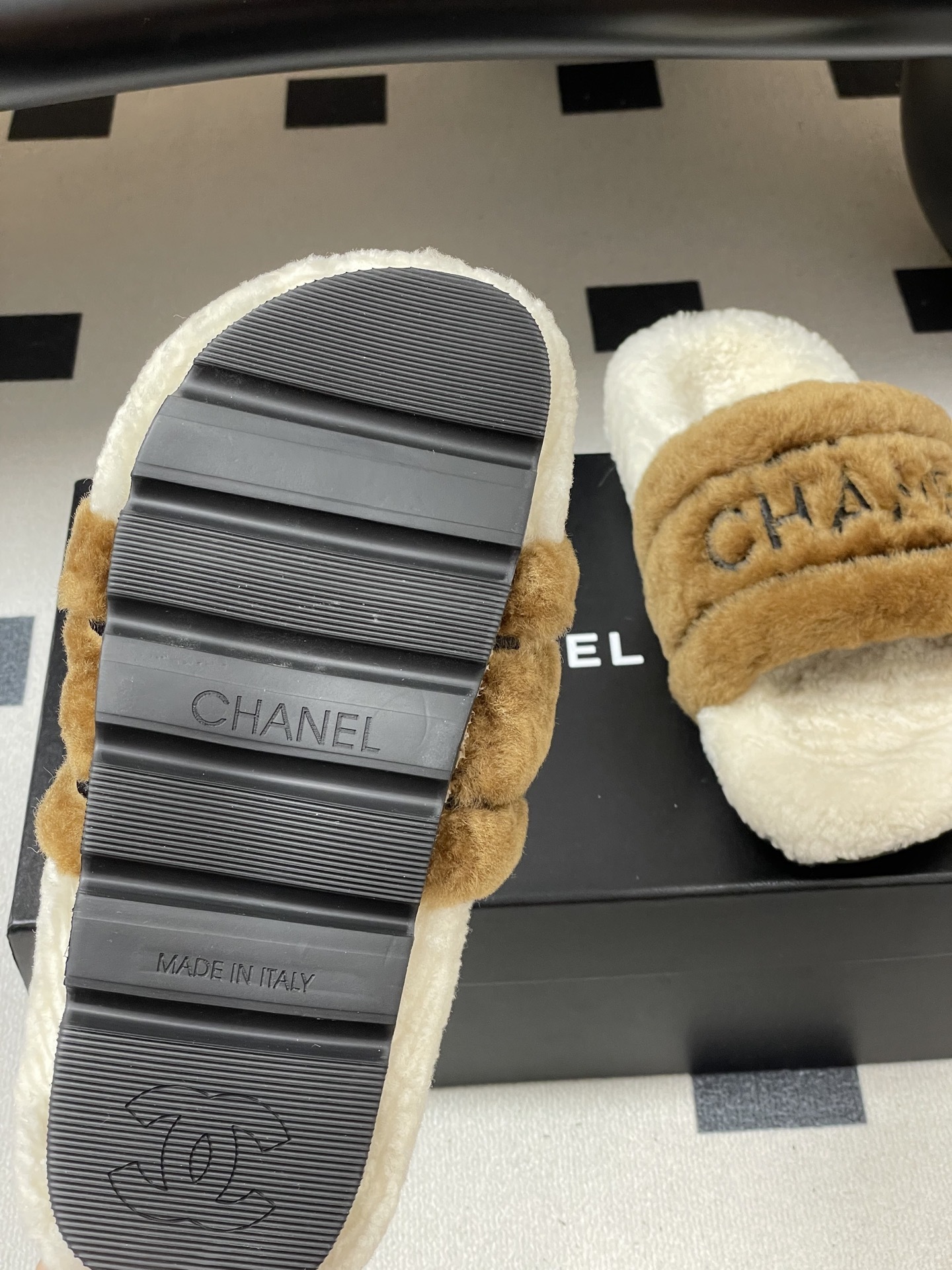A pair of Chanel branded faux fur slides in brown and white shearling on a black surface. - Hình 8