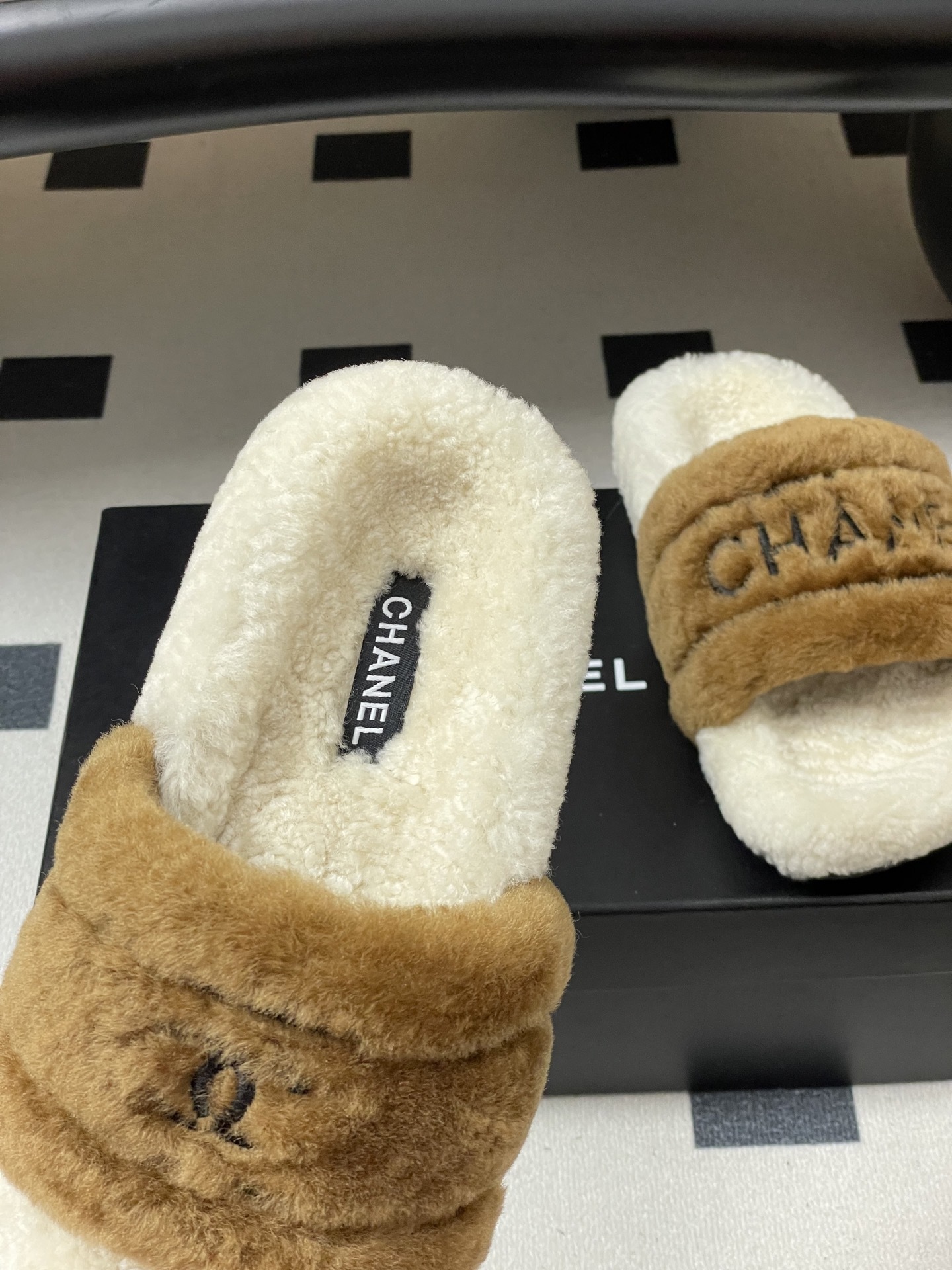 A pair of Chanel branded faux fur slides in brown and white shearling on a black surface. - Hình 7