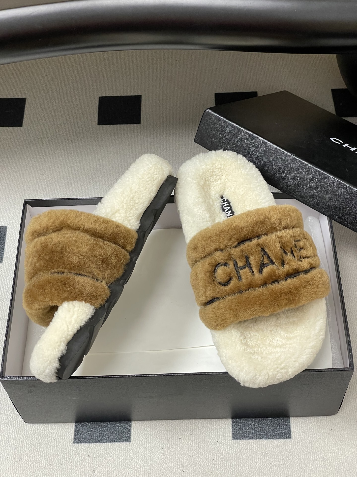 A pair of Chanel branded faux fur slides in brown and white shearling on a black surface. - Hình 6