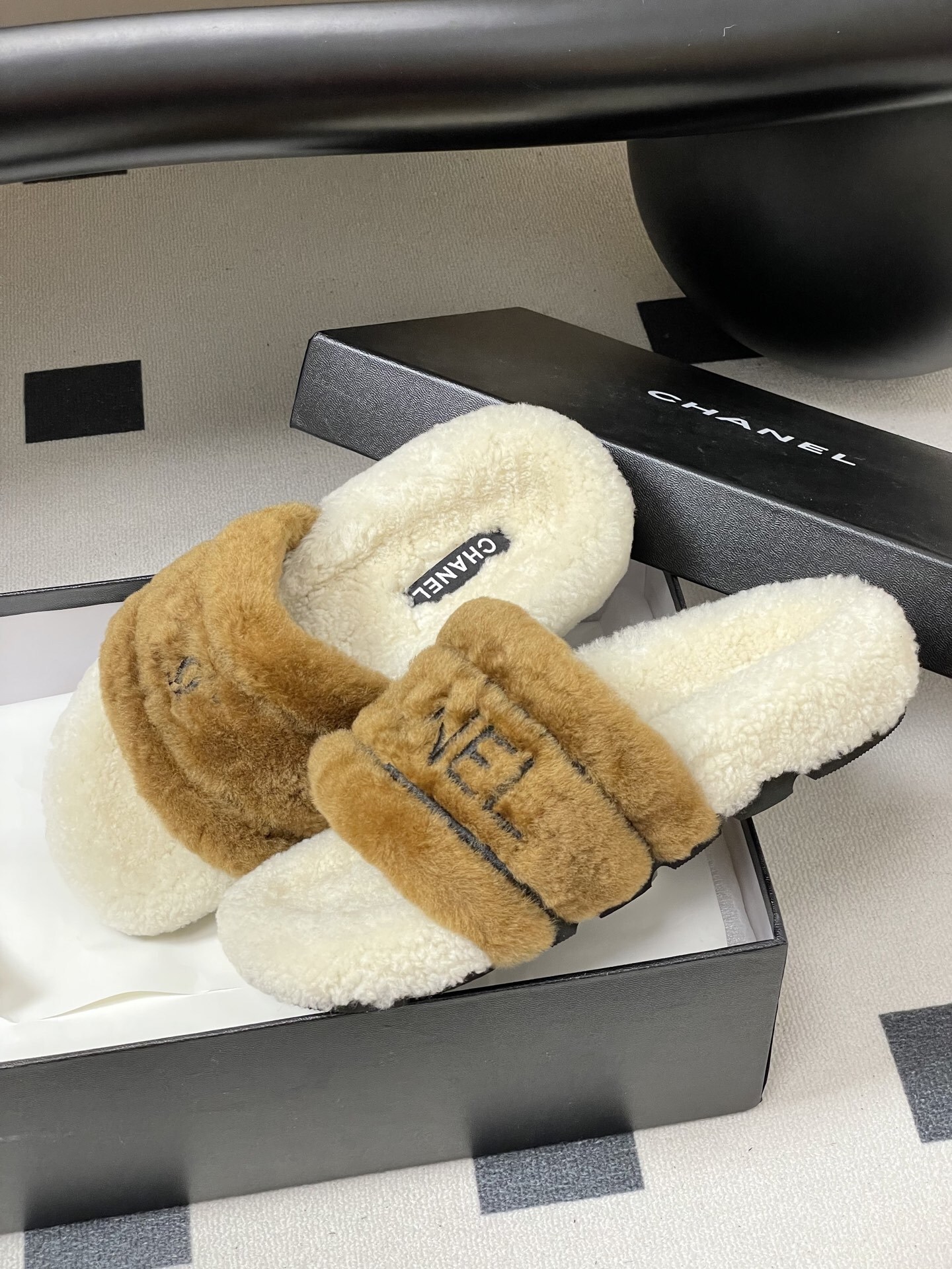 A pair of Chanel branded faux fur slides in brown and white shearling on a black surface. - Hình 4