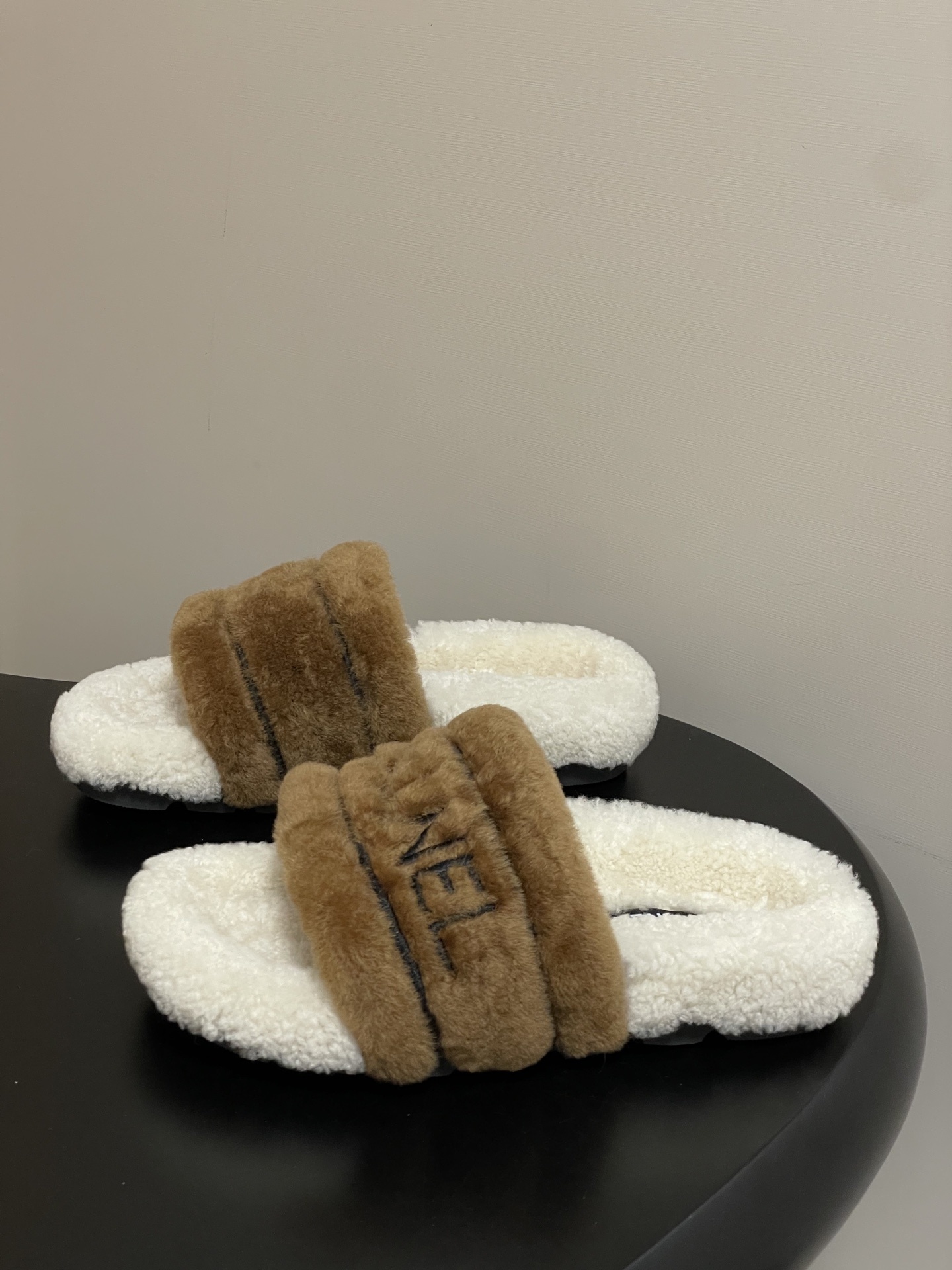 A pair of Chanel branded faux fur slides in brown and white shearling on a black surface. - Hình 3