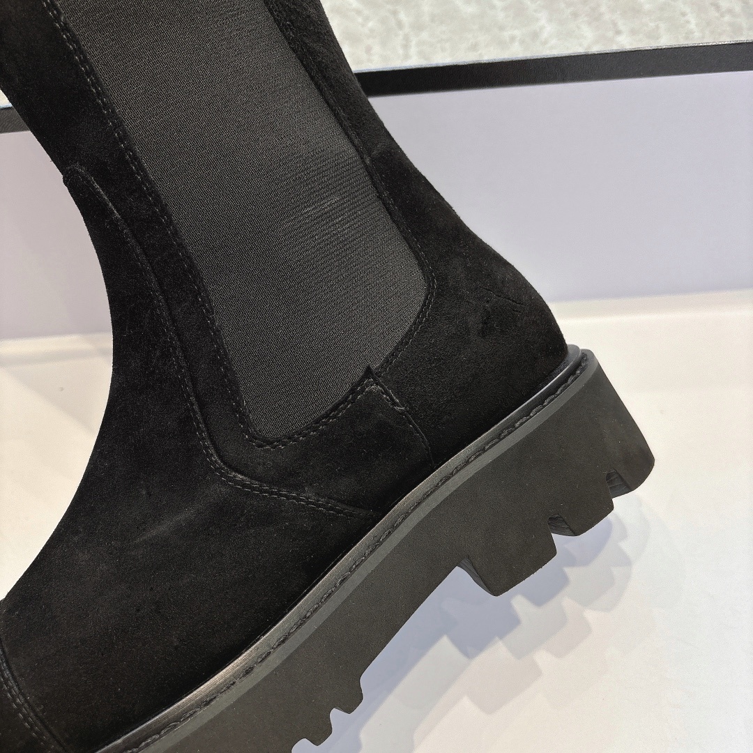 Pair of black suede knee-high boots with chunky lug soles and elastic side panels on a display box - Hình 8