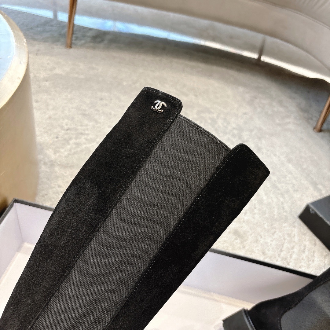 Pair of black suede knee-high boots with chunky lug soles and elastic side panels on a display box - Hình 7