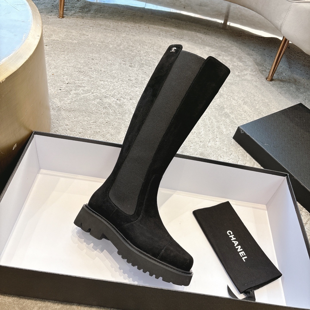 Pair of black suede knee-high boots with chunky lug soles and elastic side panels on a display box - Hình 5