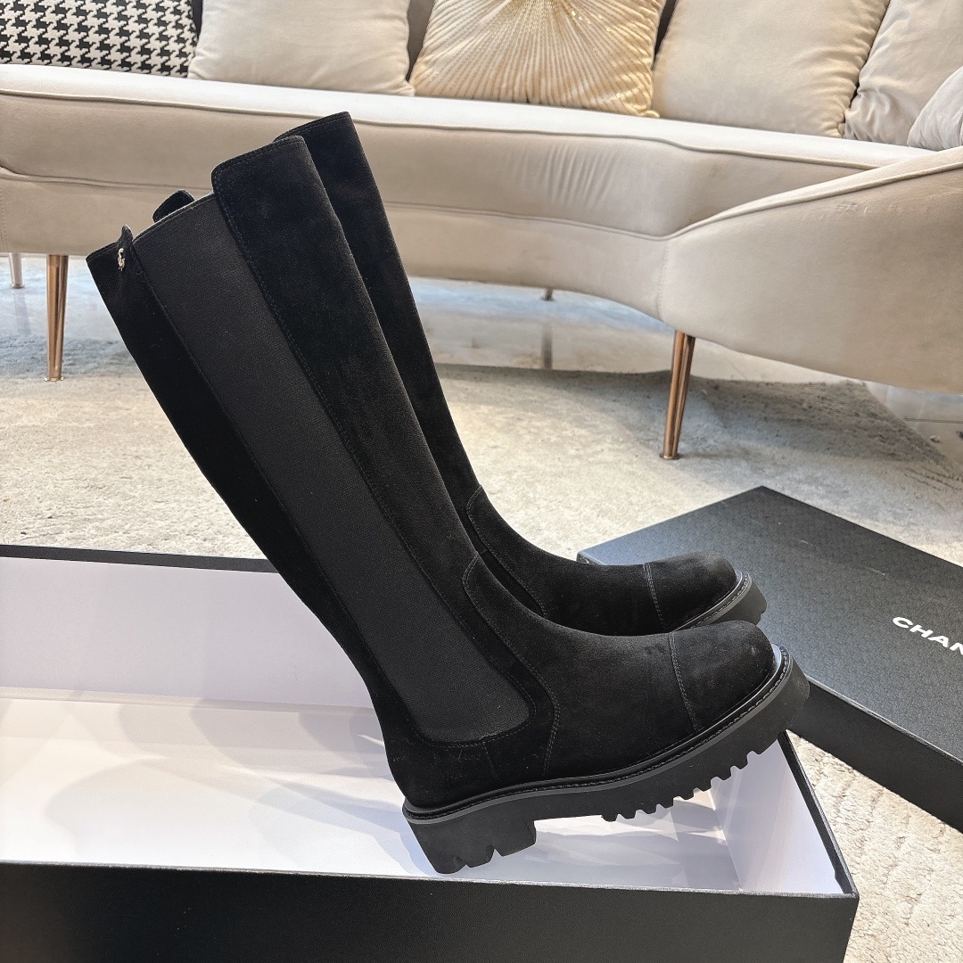 Pair of black suede knee-high boots with chunky lug soles and elastic side panels on a display box - Hình 4
