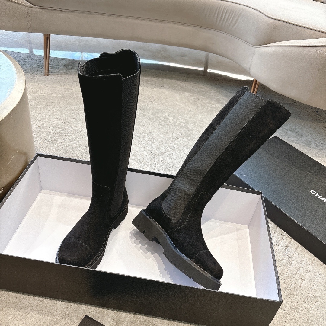 Pair of black suede knee-high boots with chunky lug soles and elastic side panels on a display box - Hình 3