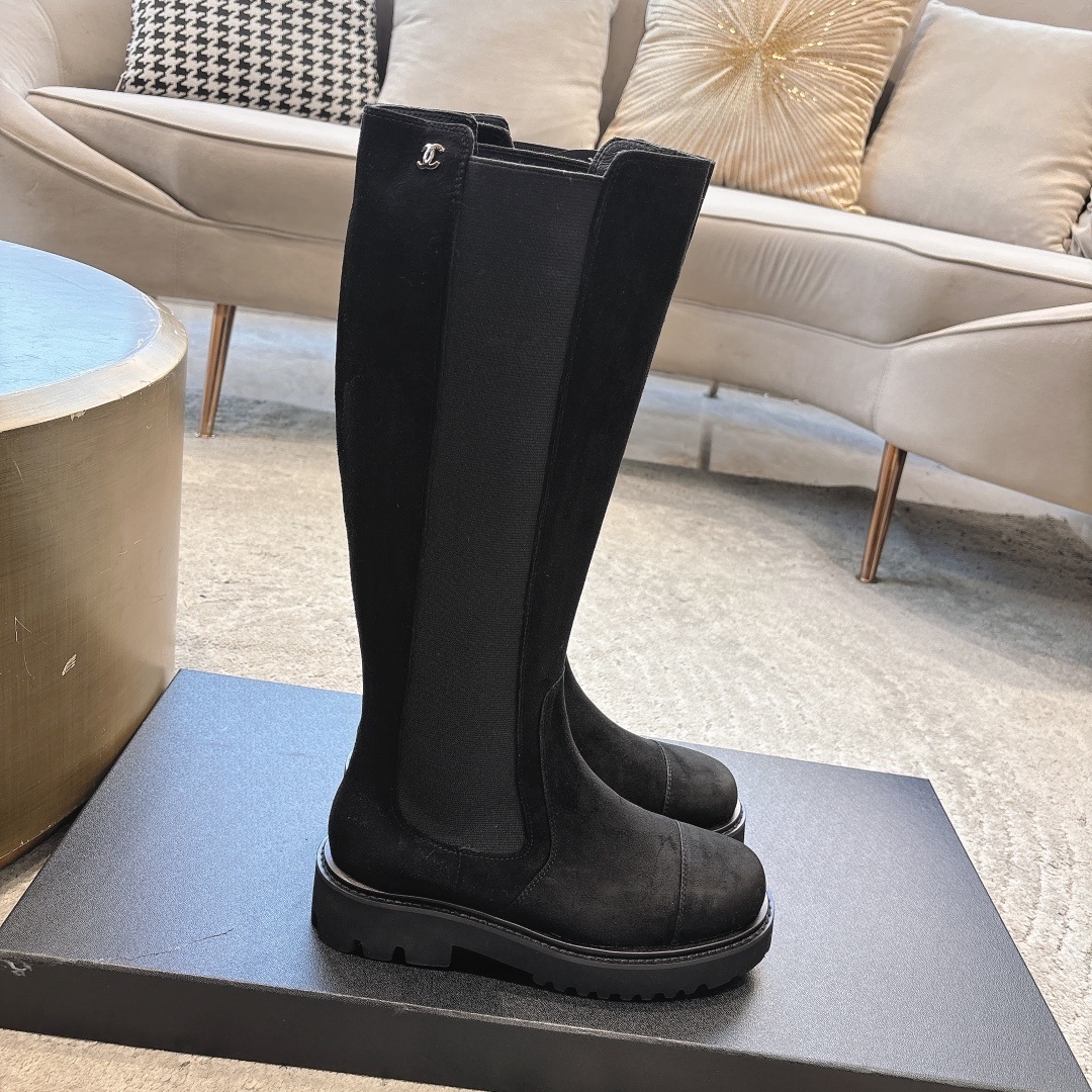 Pair of black suede knee-high boots with chunky lug soles and elastic side panels on a display box - Hình 2