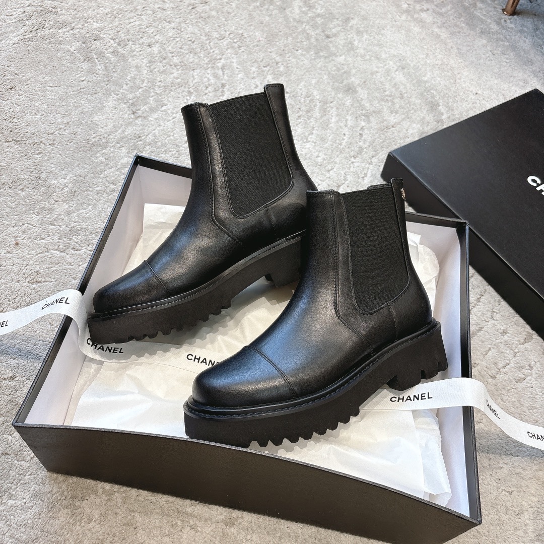 A pair of high-end black leather Chelsea boots with thick lug soles shown in a designer box with white ribbons. - Hình 5