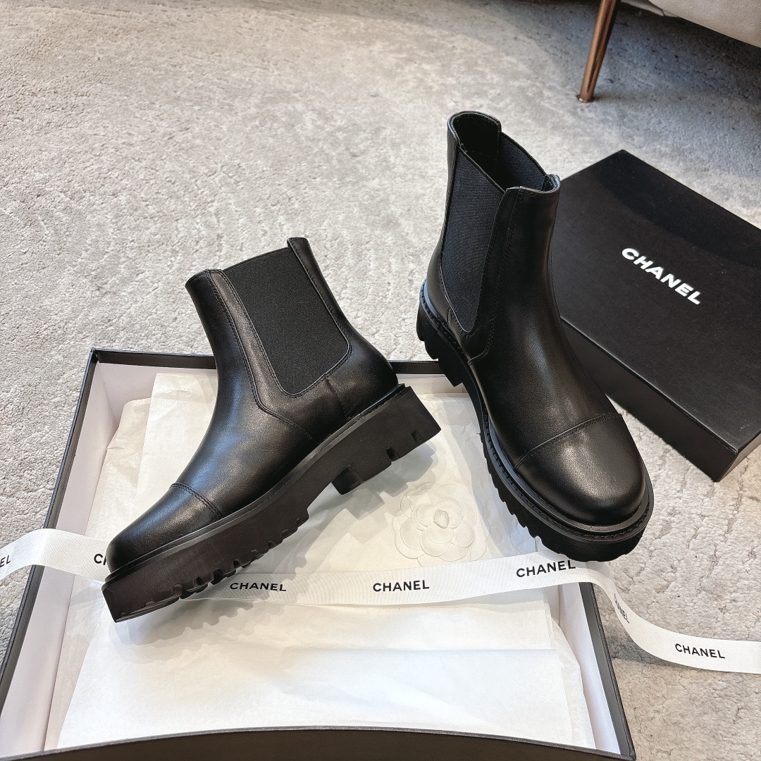 A pair of high-end black leather Chelsea boots with thick lug soles shown in a designer box with white ribbons. - Hình 4