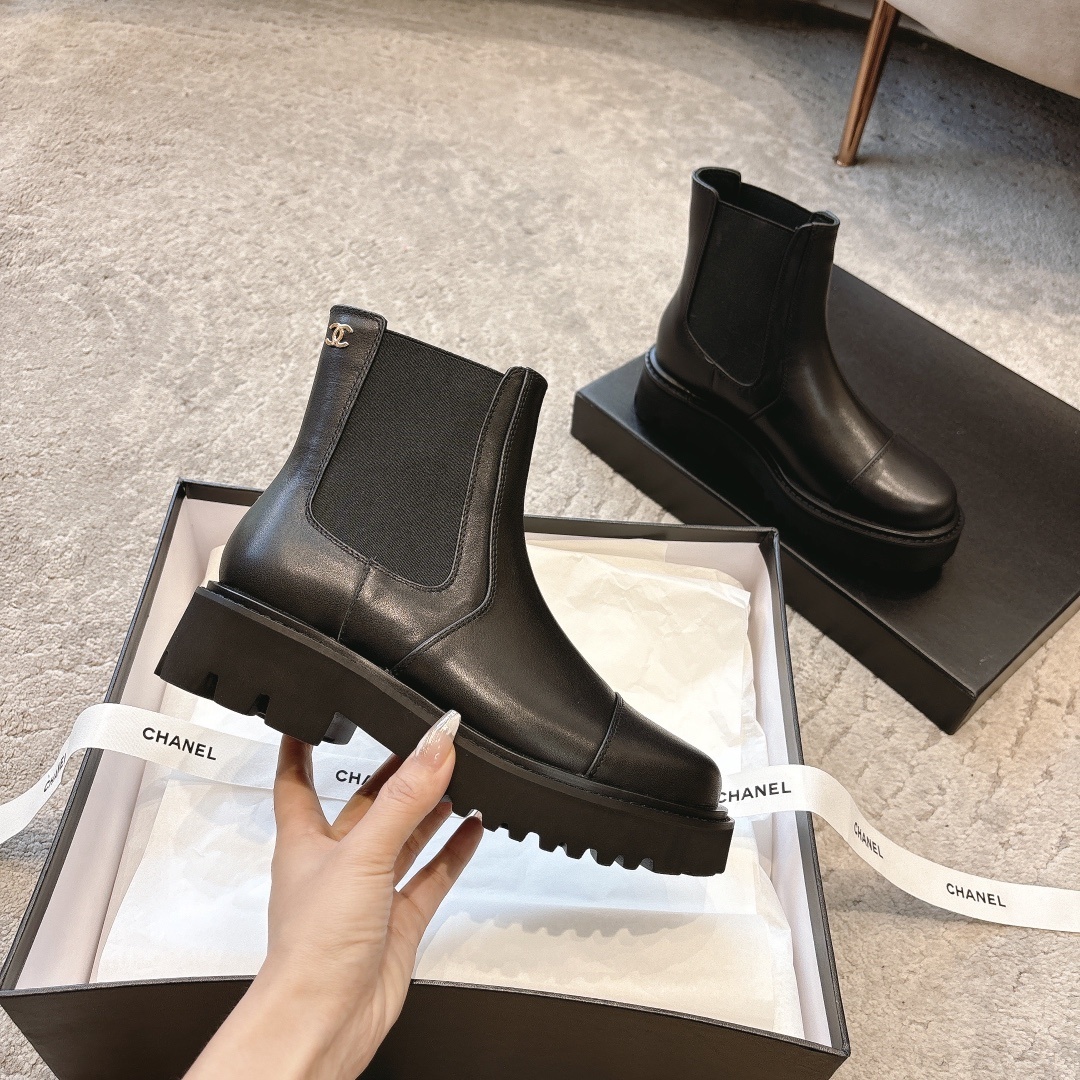 A pair of high-end black leather Chelsea boots with thick lug soles shown in a designer box with white ribbons. - Hình 2