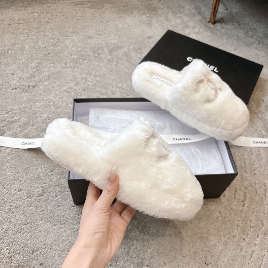 A pair of plush white faux fur slippers with a designer logo embroidery in a black gift box with white ribbon. - Hình 3