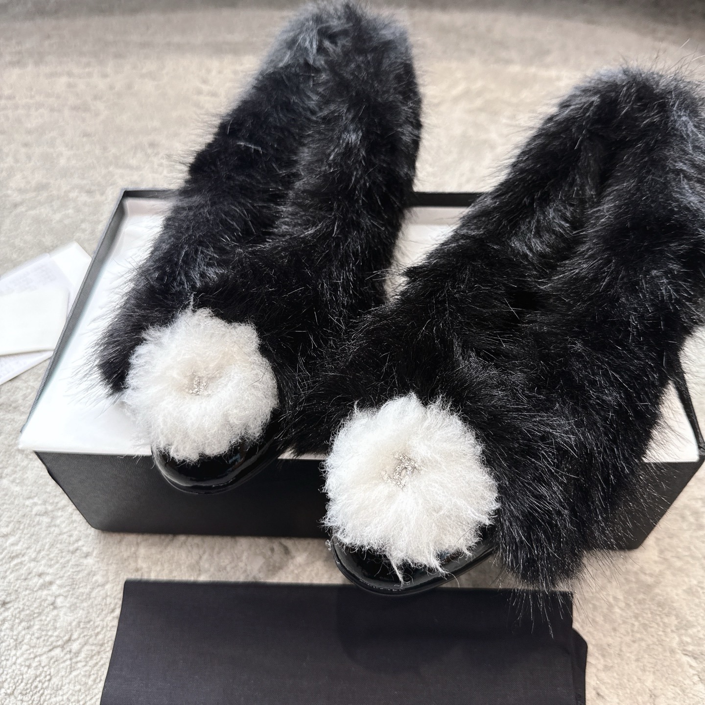 Top view of black Chanel fur loafers with white pom-poms on a grey carpet - Hình 7