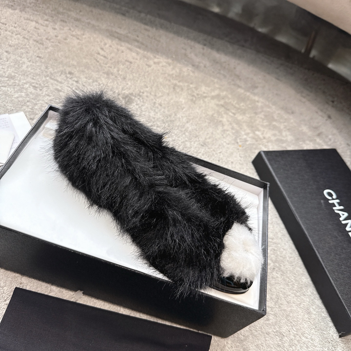 Top view of black Chanel fur loafers with white pom-poms on a grey carpet - Hình 4