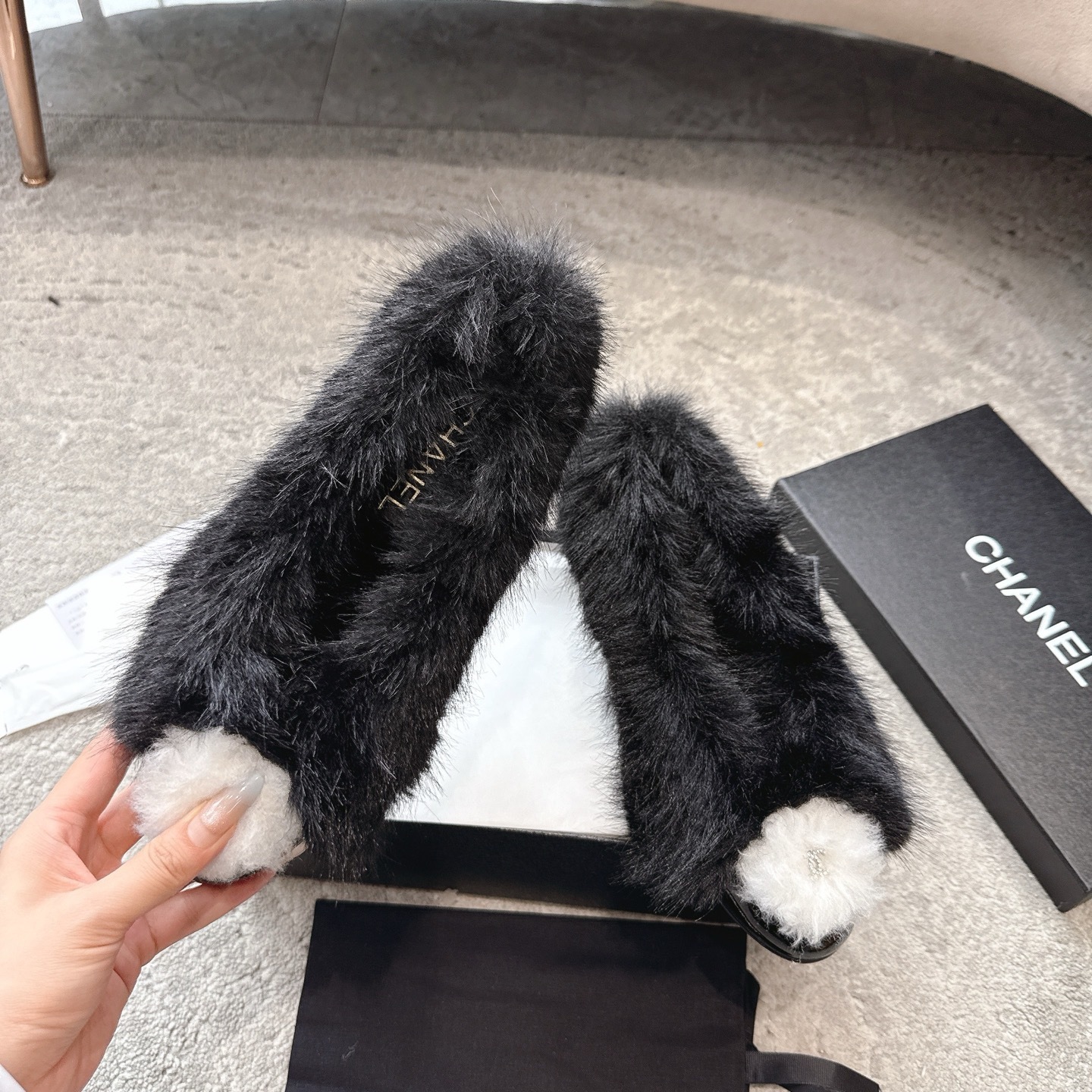 Top view of black Chanel fur loafers with white pom-poms on a grey carpet - Hình 2