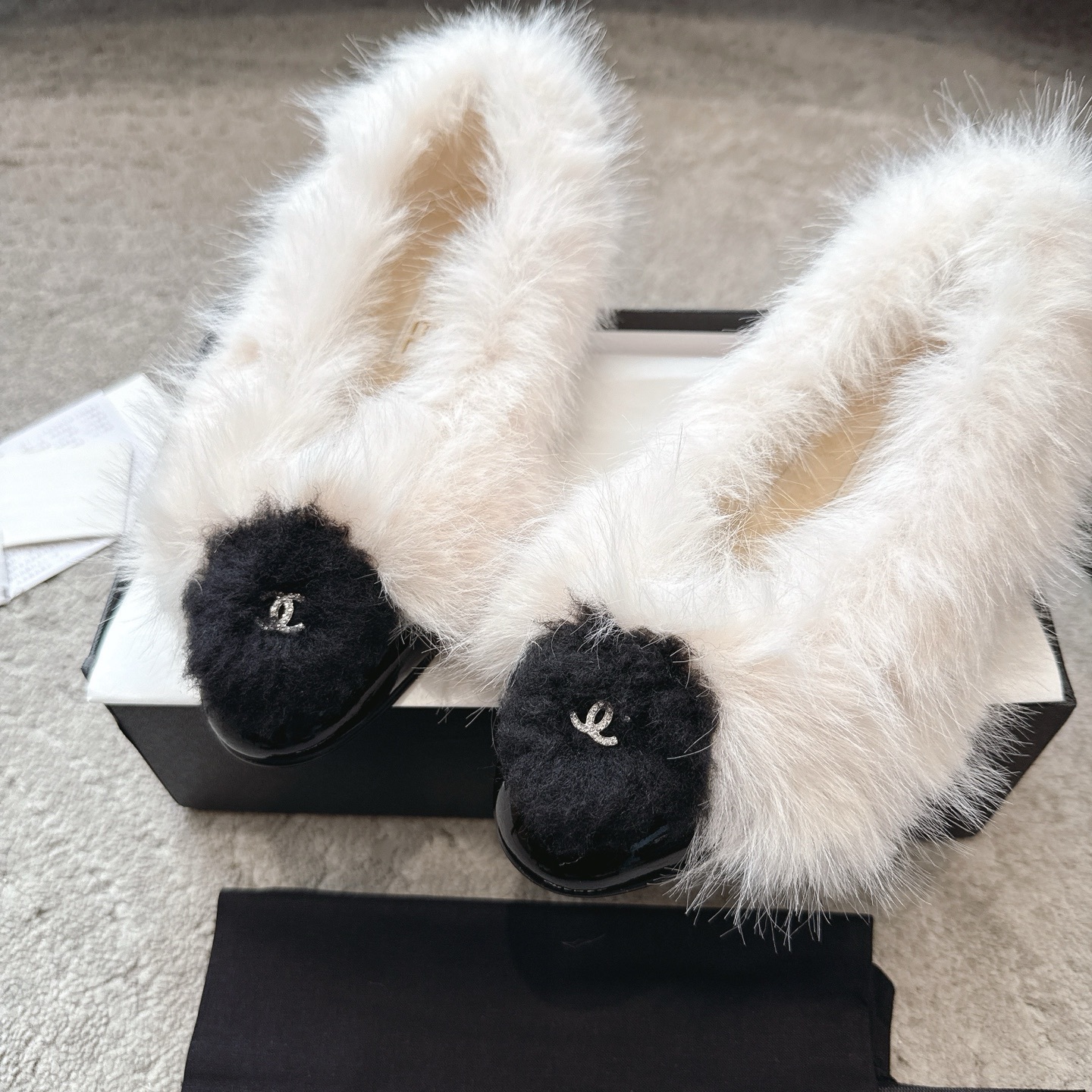 A pair of luxury white faux fur ballerina flats with black toe caps and silver CC logos, presented in a designer box. - Hình 7