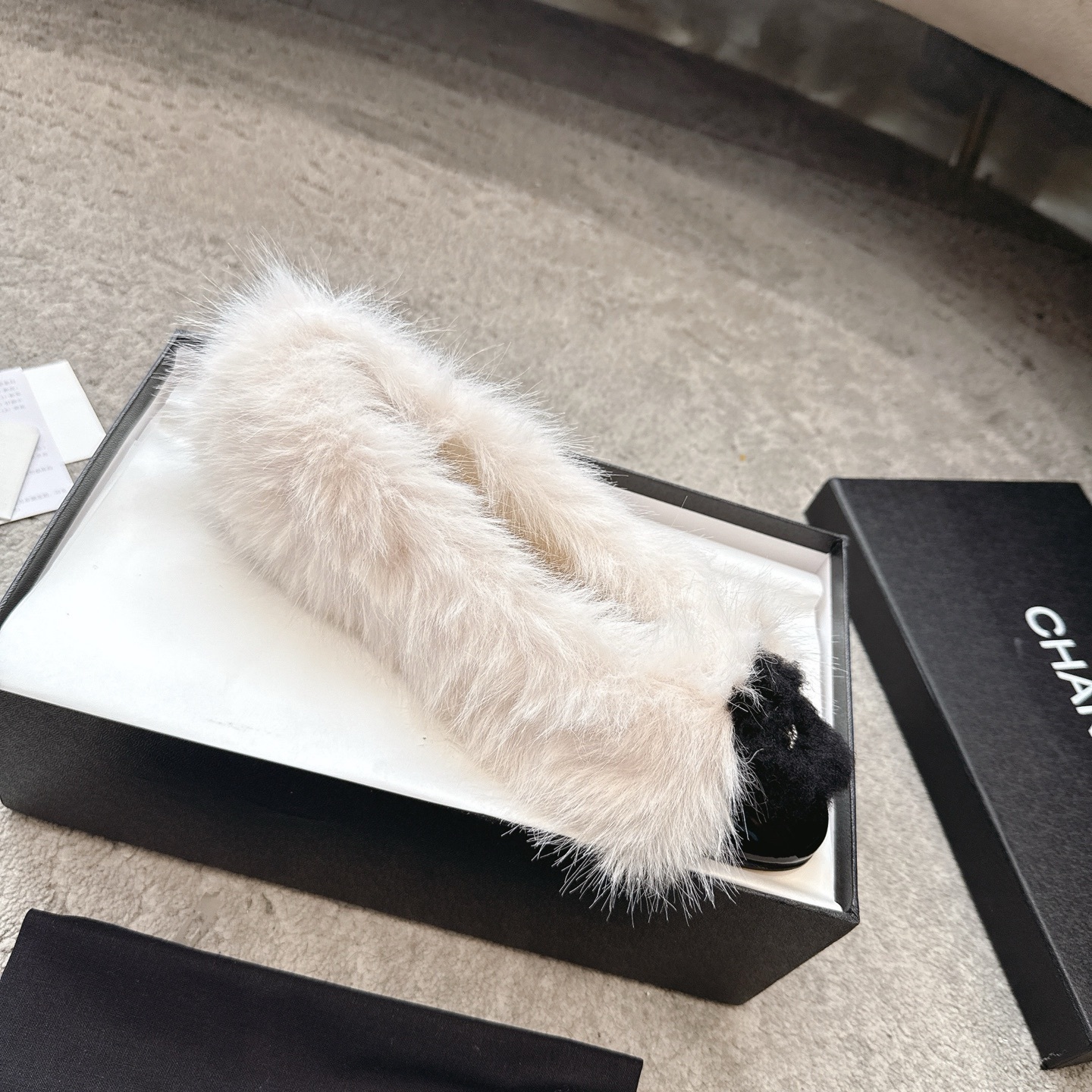 A pair of luxury white faux fur ballerina flats with black toe caps and silver CC logos, presented in a designer box. - Hình 4
