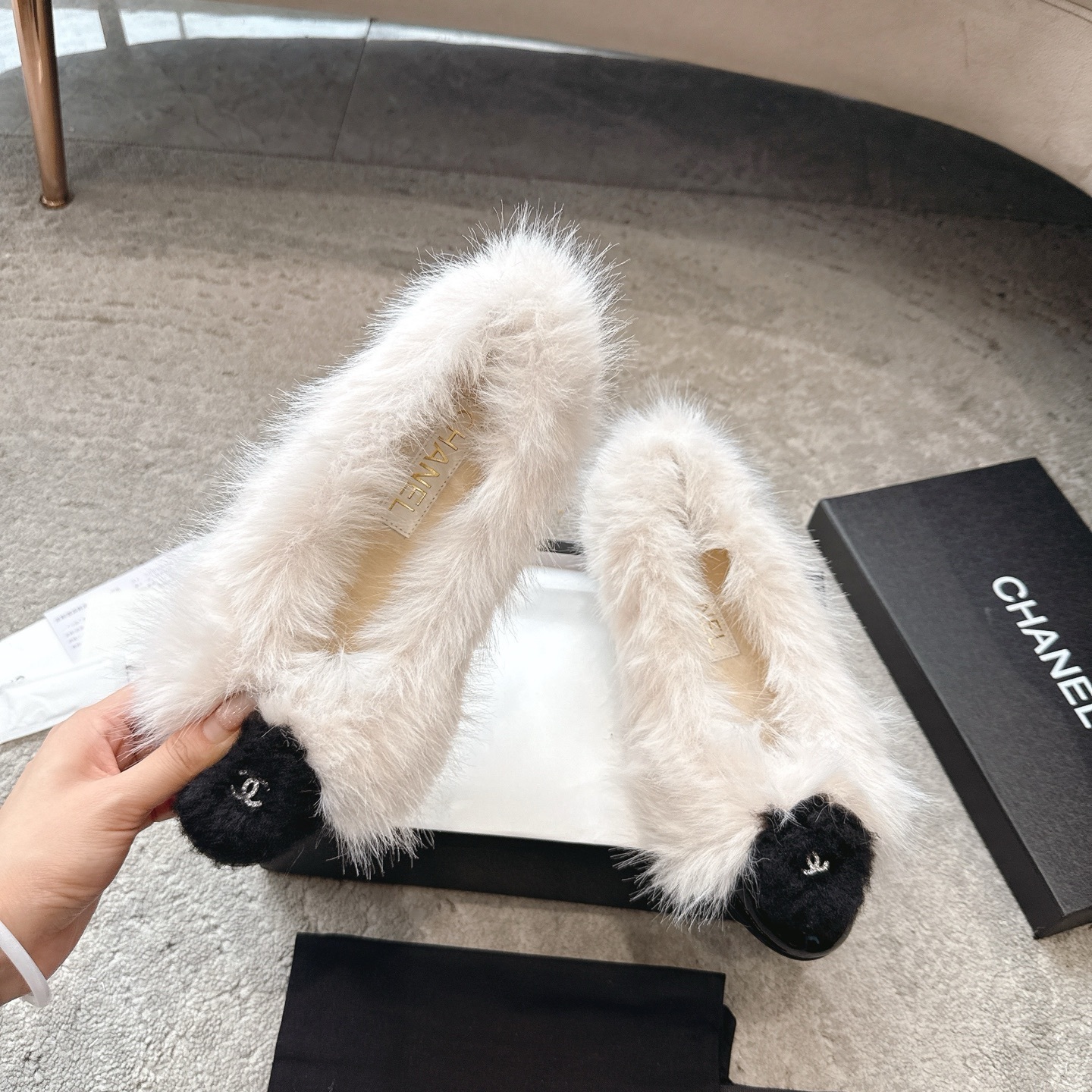 A pair of luxury white faux fur ballerina flats with black toe caps and silver CC logos, presented in a designer box. - Hình 2