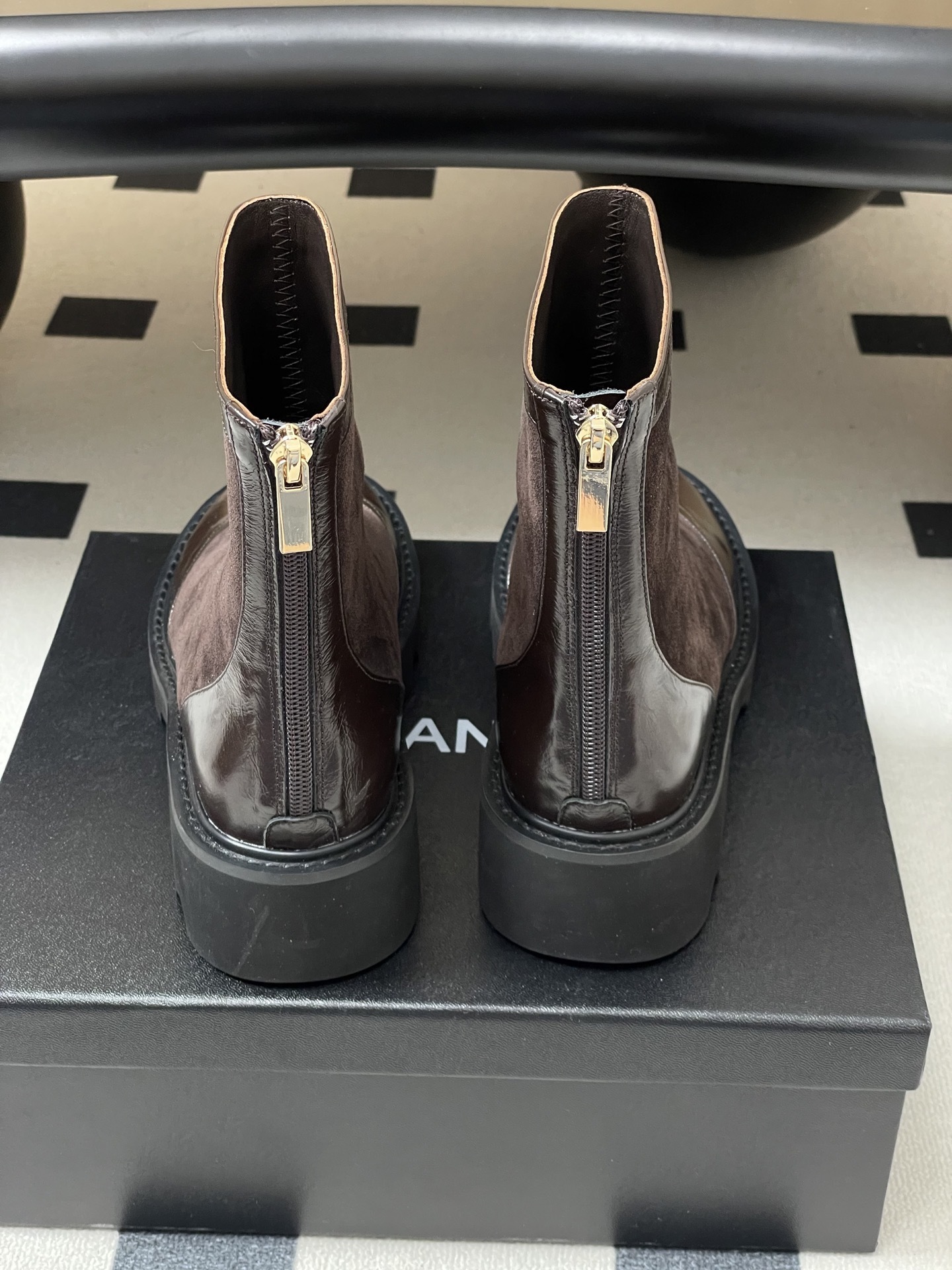 A pair of Chanel dark brown suede and leather ankle boots with gold CC logos and thick black lug soles on a black table. - Hình 9