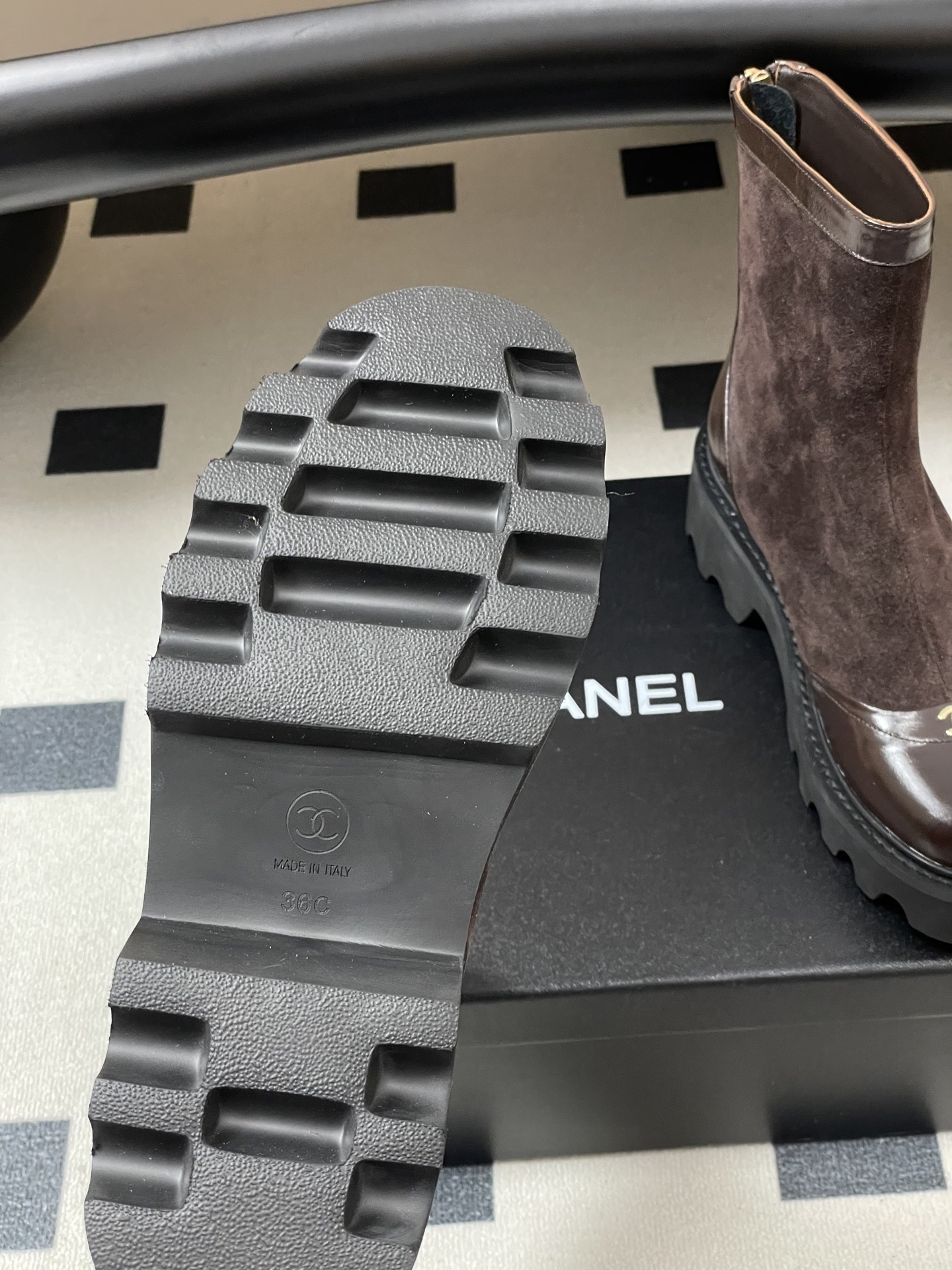 A pair of Chanel dark brown suede and leather ankle boots with gold CC logos and thick black lug soles on a black table. - Hình 8