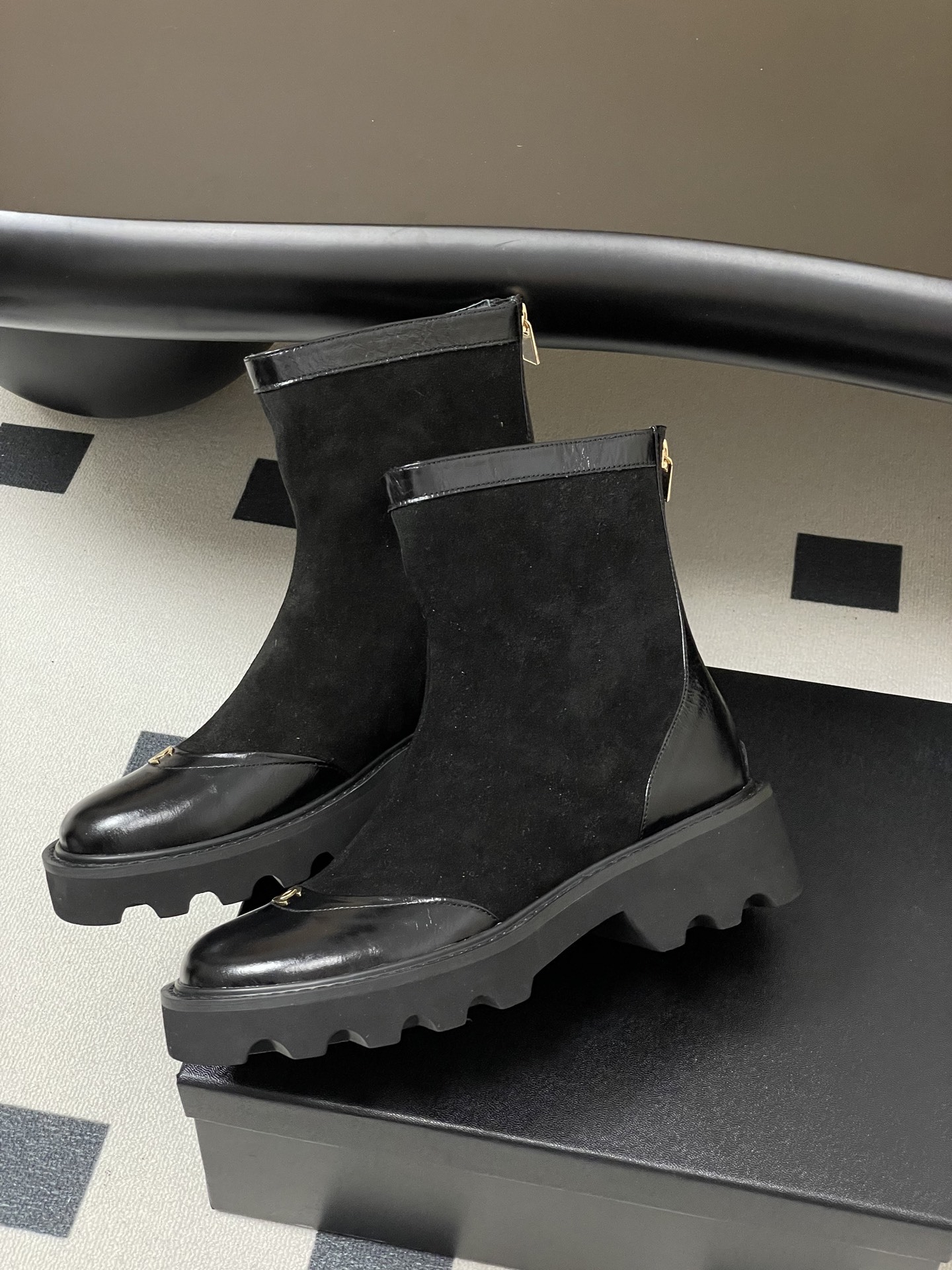 A pair of Chanel black suede ankle boots with patent leather toe caps, gold CC logos, and chunky lug soles. - Hình 4