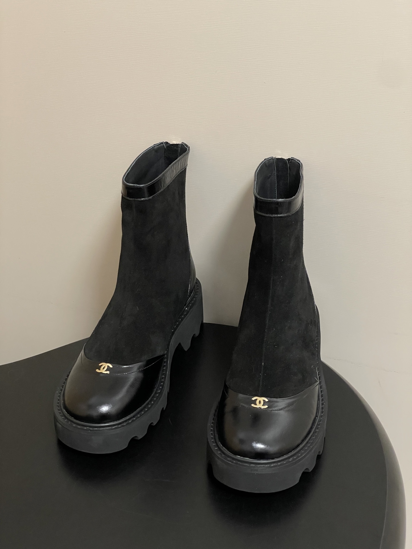 A pair of Chanel black suede ankle boots with patent leather toe caps, gold CC logos, and chunky lug soles. - Hình 2