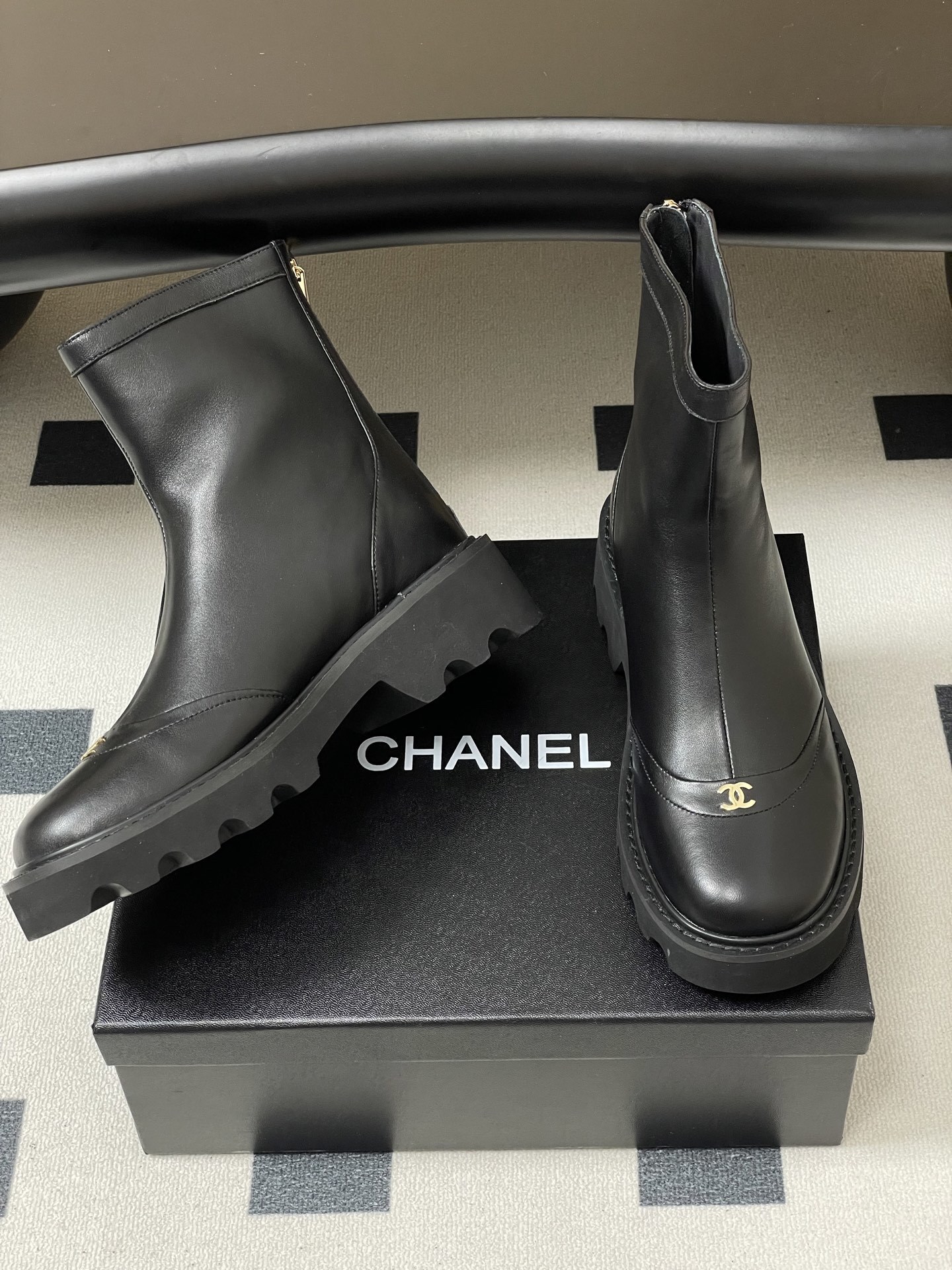 Pair of black leather ankle boots with chunky lug soles and gold interlocking logo on the toe - Hình 5
