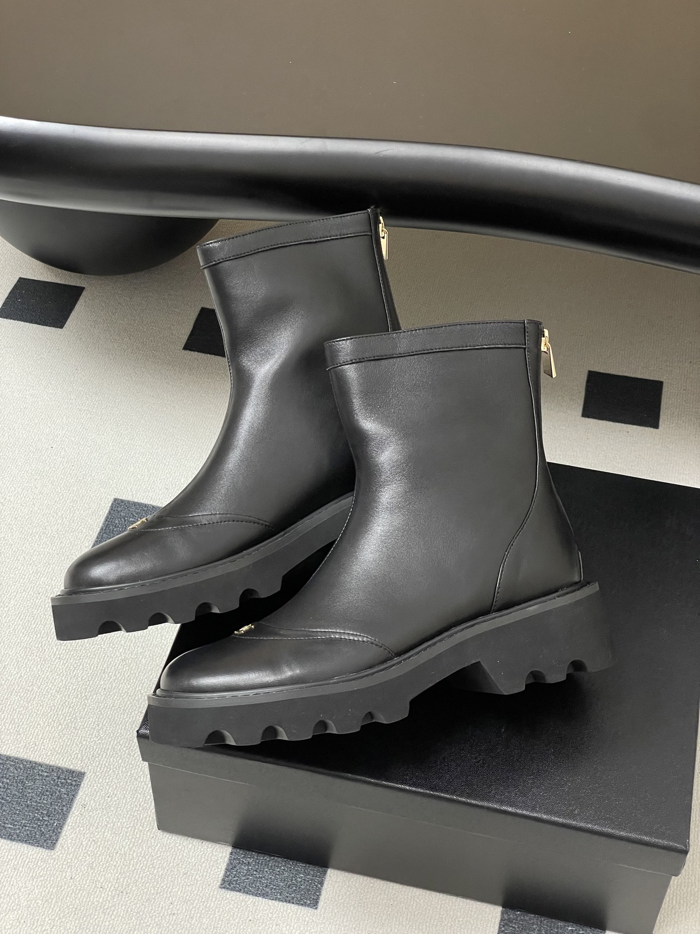 Pair of black leather ankle boots with chunky lug soles and gold interlocking logo on the toe - Hình 4
