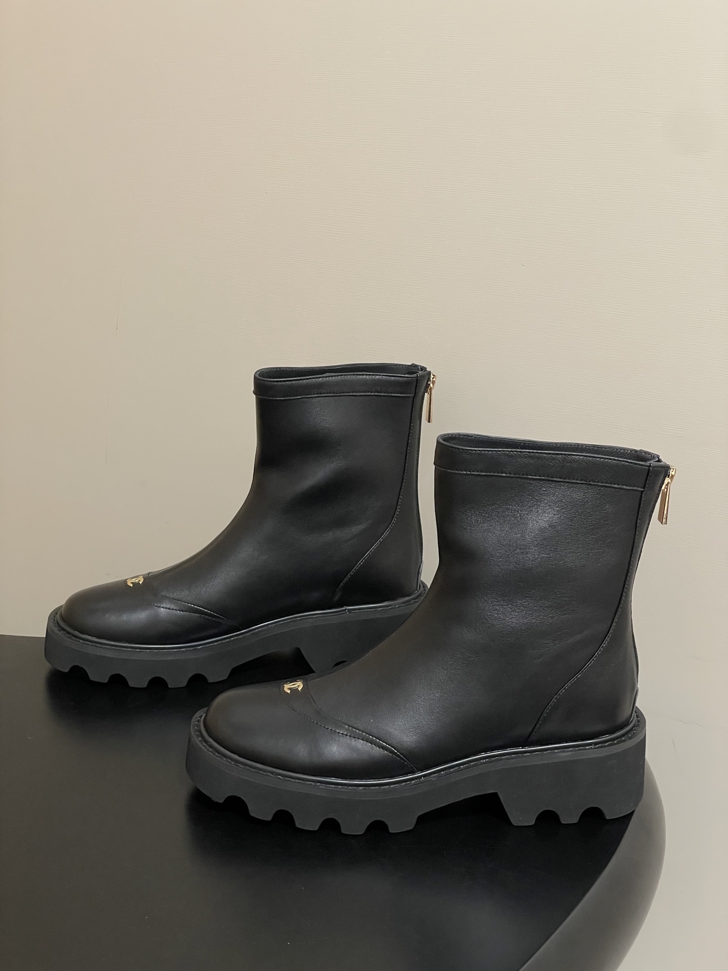 Pair of black leather ankle boots with chunky lug soles and gold interlocking logo on the toe - Hình 3