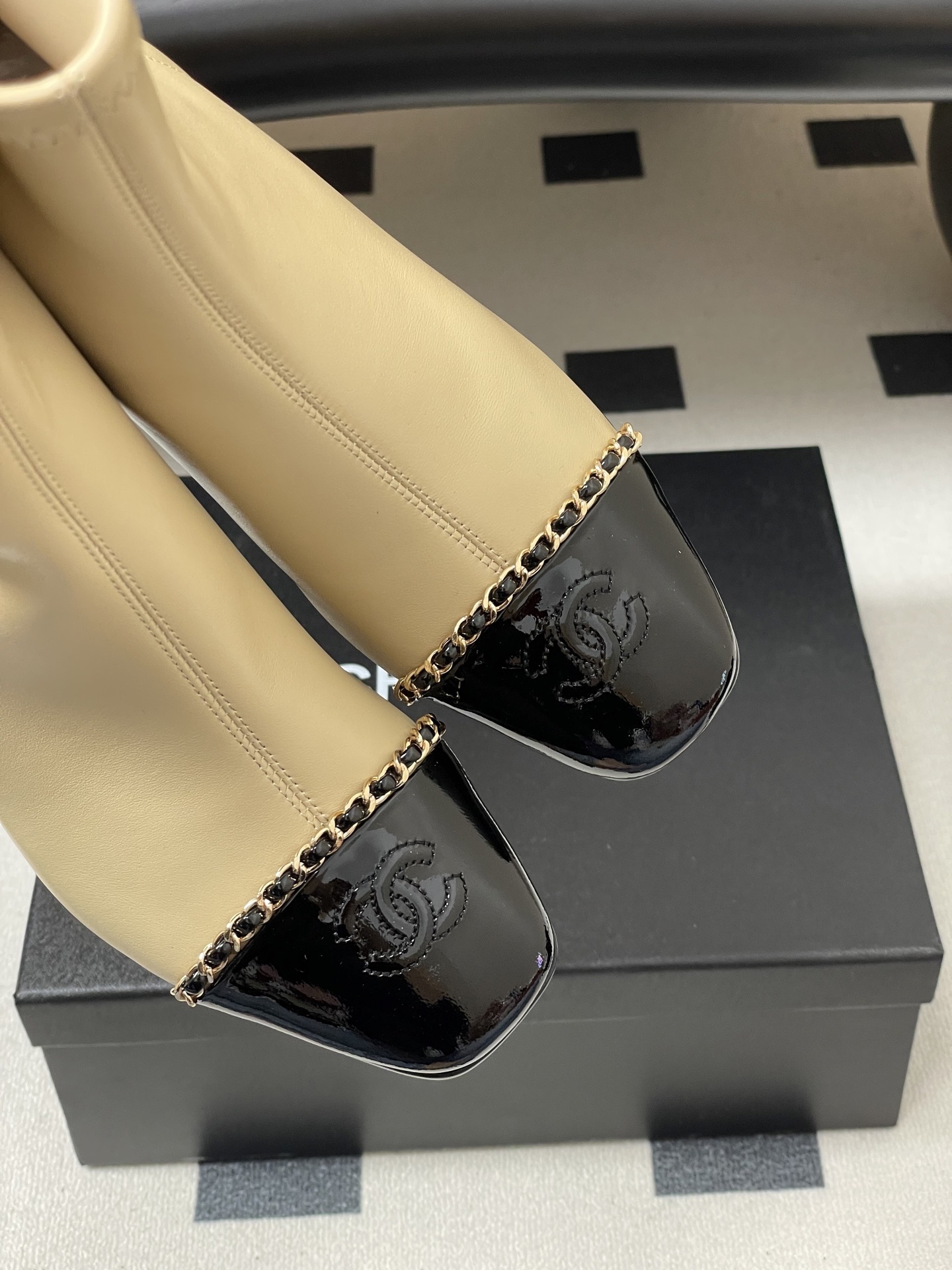 Pair of elegant beige leather ankle boots with black patent cap toes and gold chain detailing - Hình 10