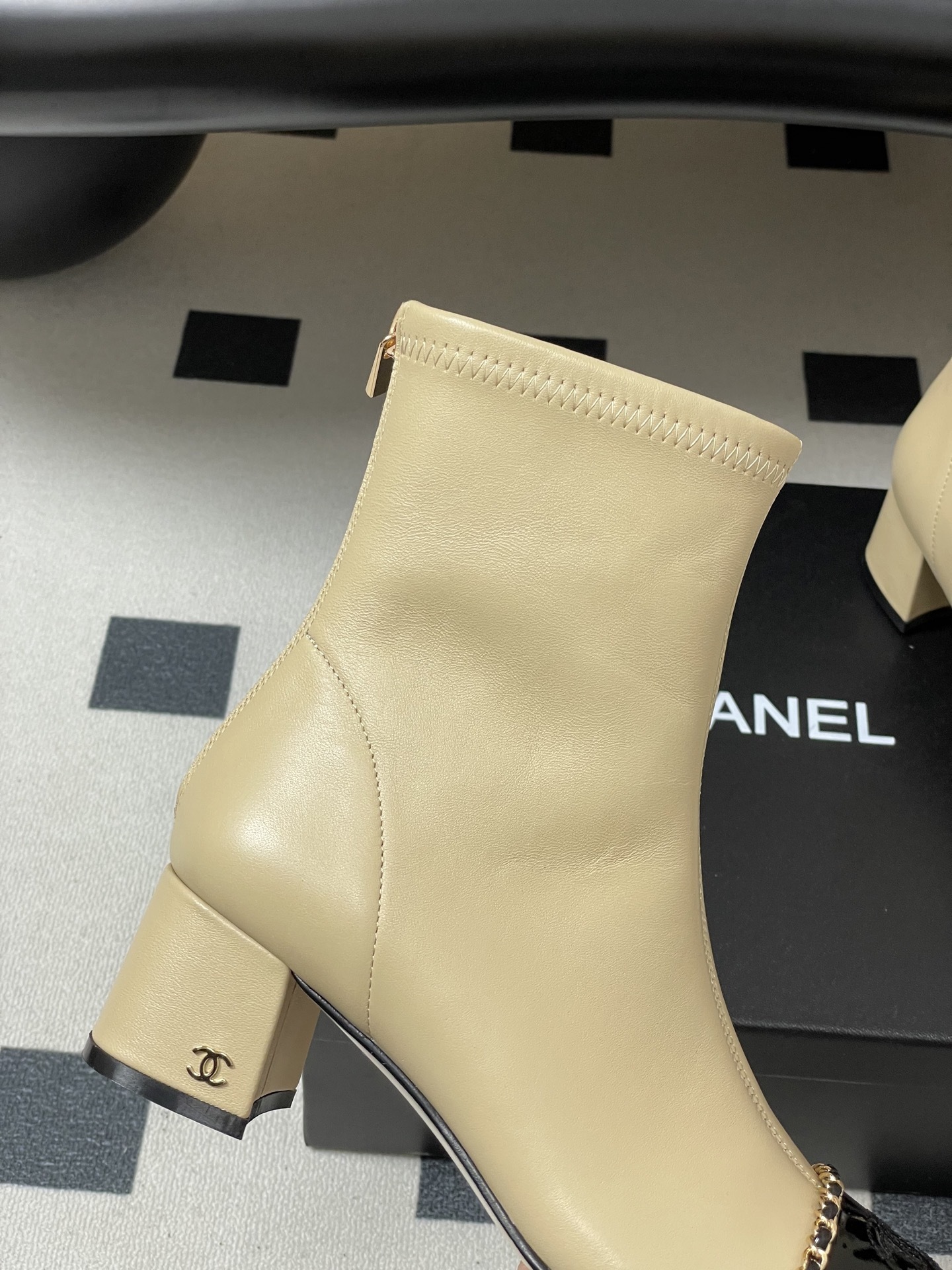 Pair of elegant beige leather ankle boots with black patent cap toes and gold chain detailing - Hình 9