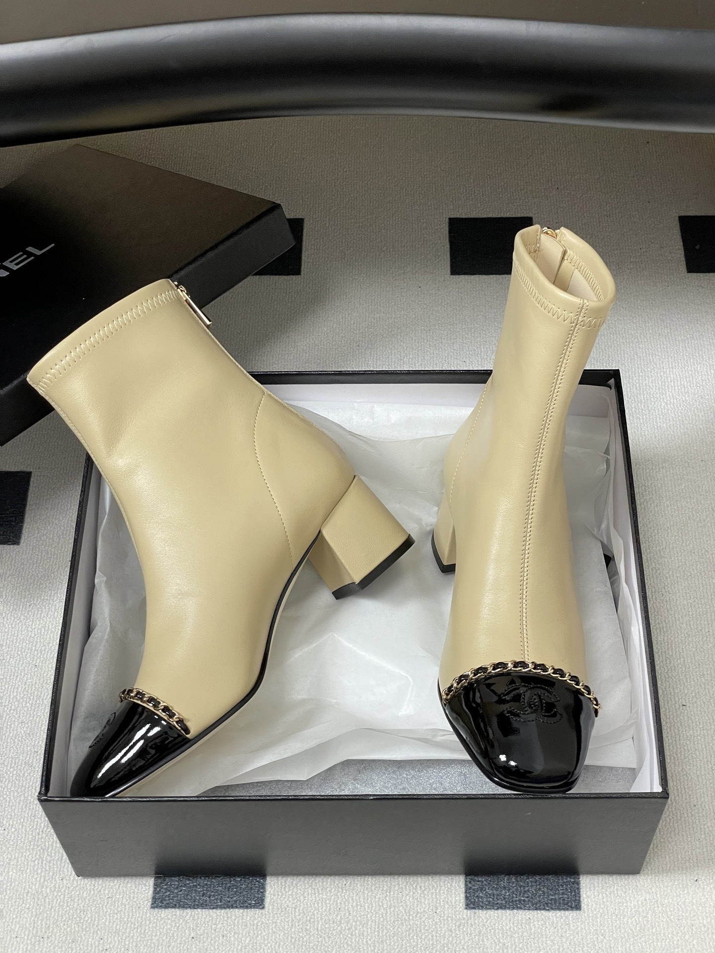 Pair of elegant beige leather ankle boots with black patent cap toes and gold chain detailing - Hình 7