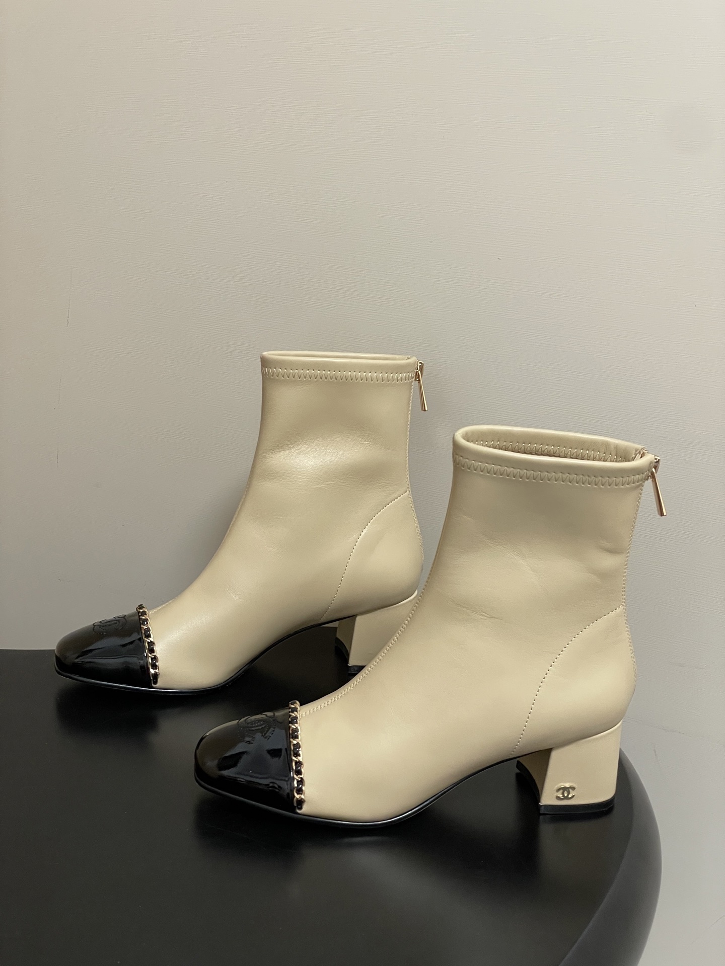 Pair of elegant beige leather ankle boots with black patent cap toes and gold chain detailing - Hình 4