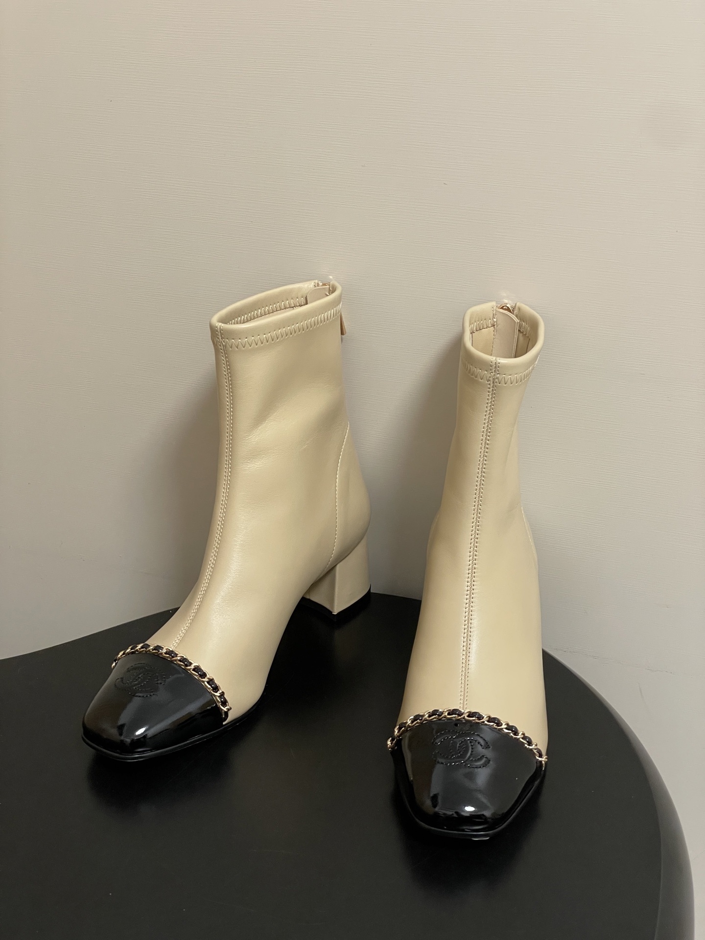 Pair of elegant beige leather ankle boots with black patent cap toes and gold chain detailing - Hình 3
