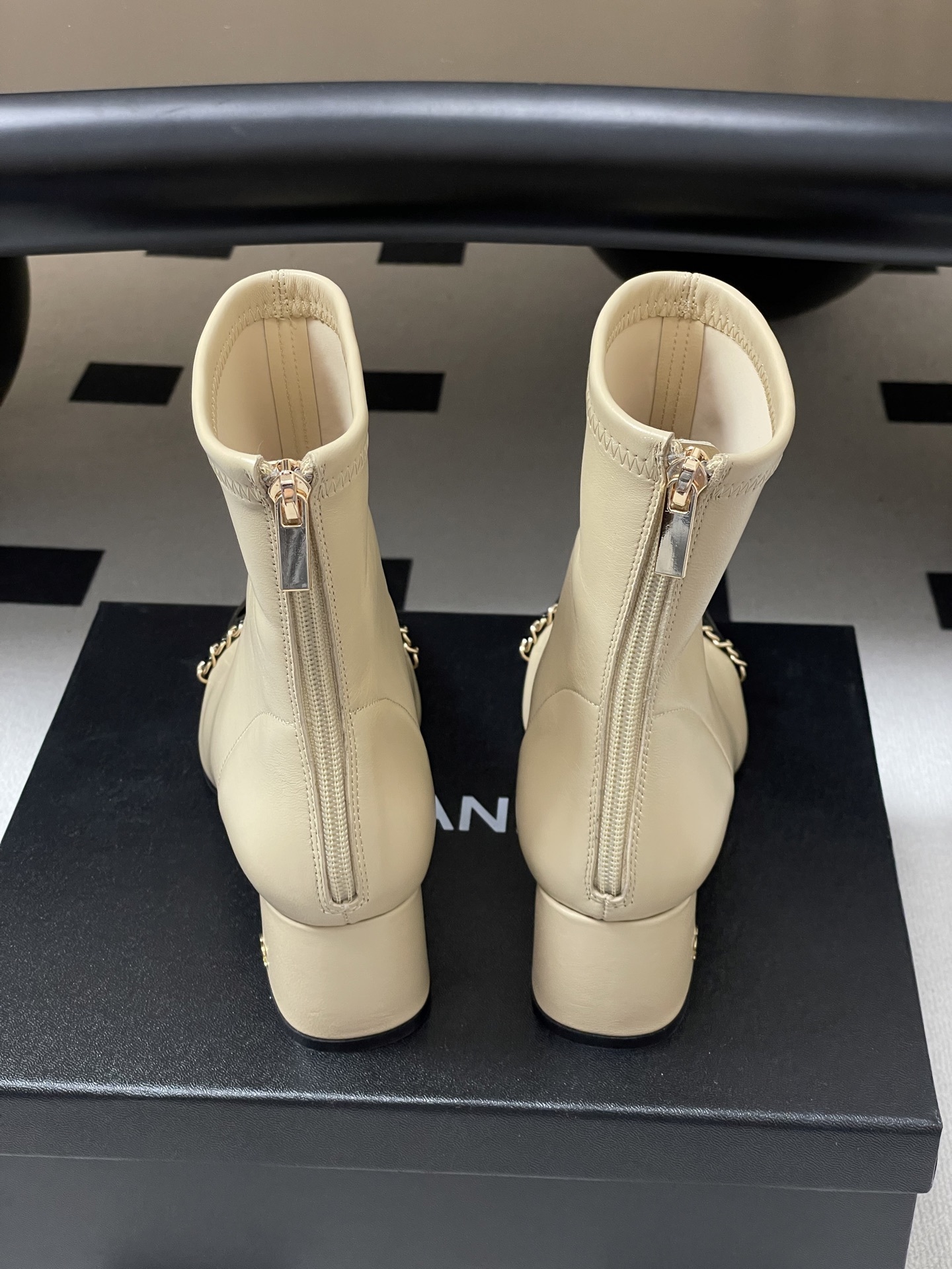 Pair of elegant beige leather ankle boots with black patent cap toes and gold chain detailing - Hình 2