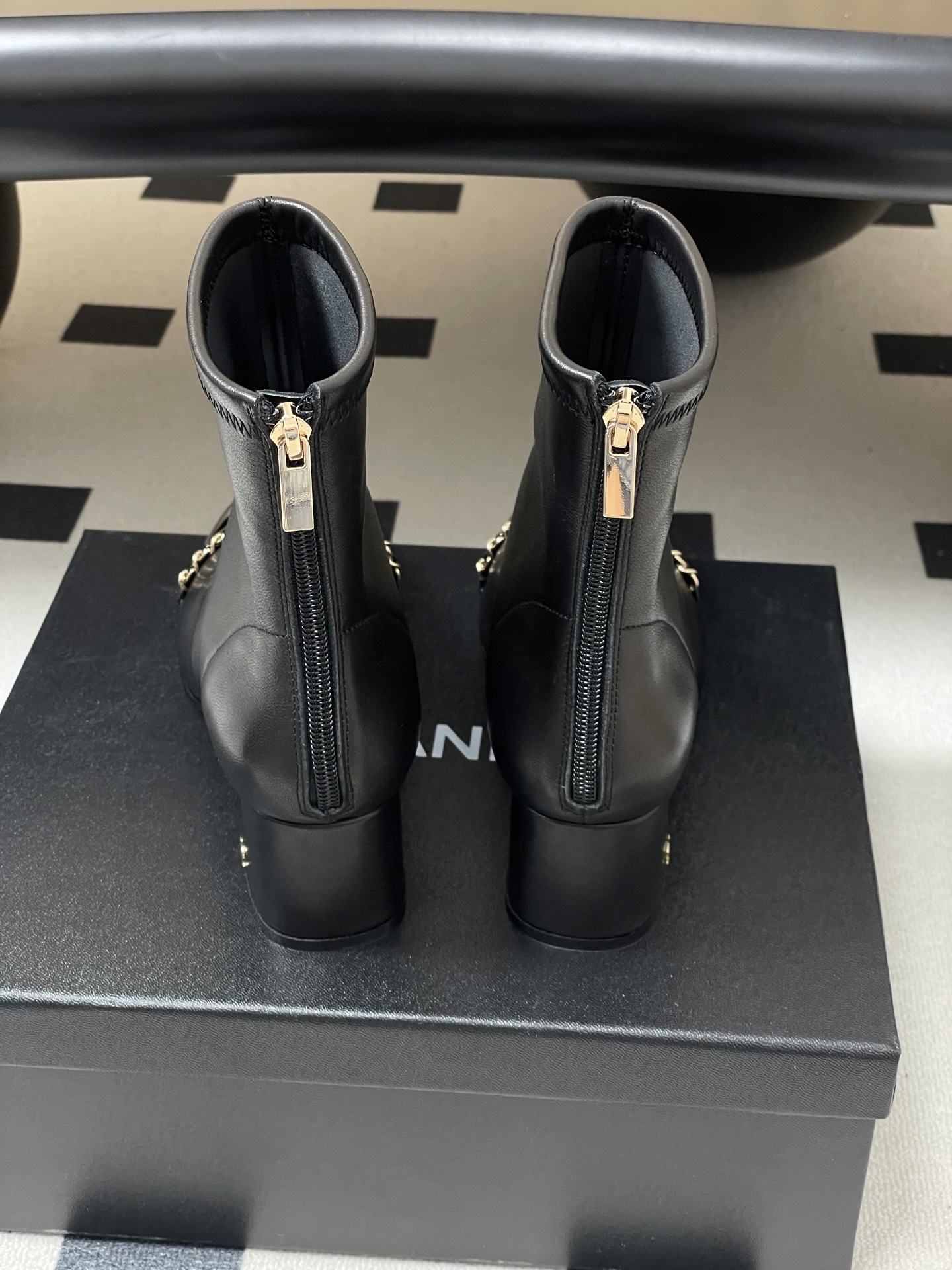 Elegant black leather ankle boots with gold chain detail and patent leather square toe cap on a black table. - Hình 9