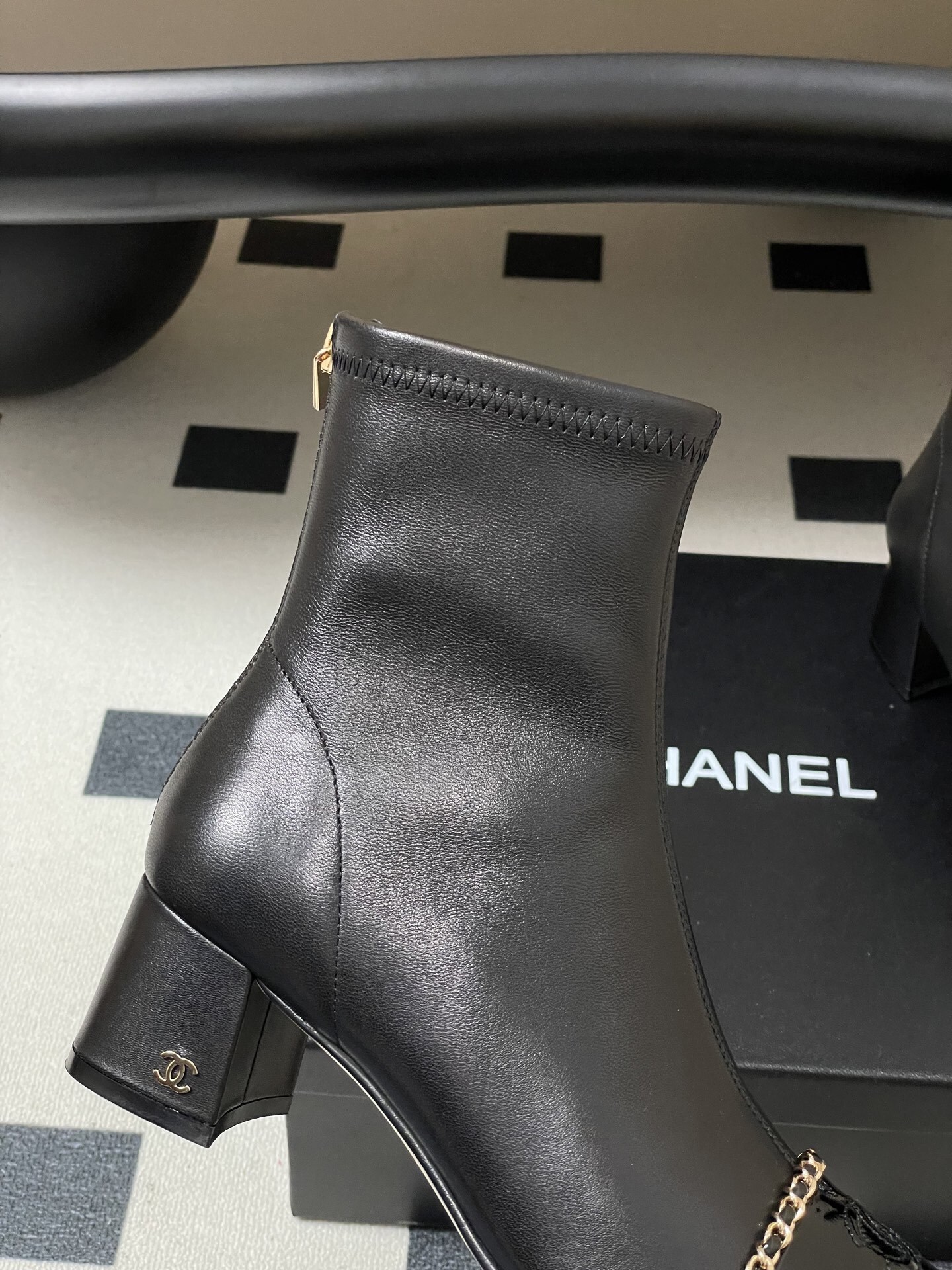 Elegant black leather ankle boots with gold chain detail and patent leather square toe cap on a black table. - Hình 7