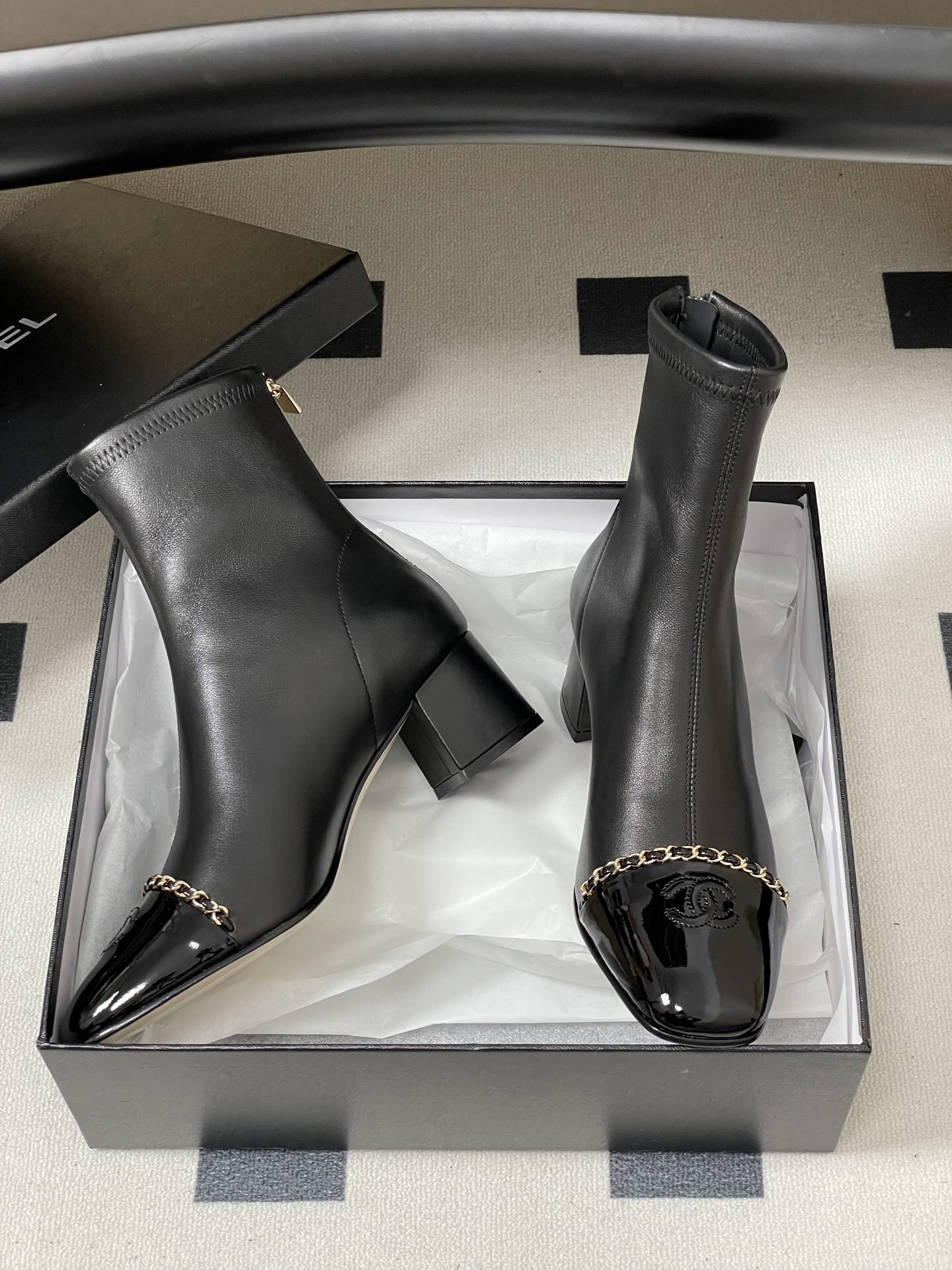 Elegant black leather ankle boots with gold chain detail and patent leather square toe cap on a black table. - Hình 6