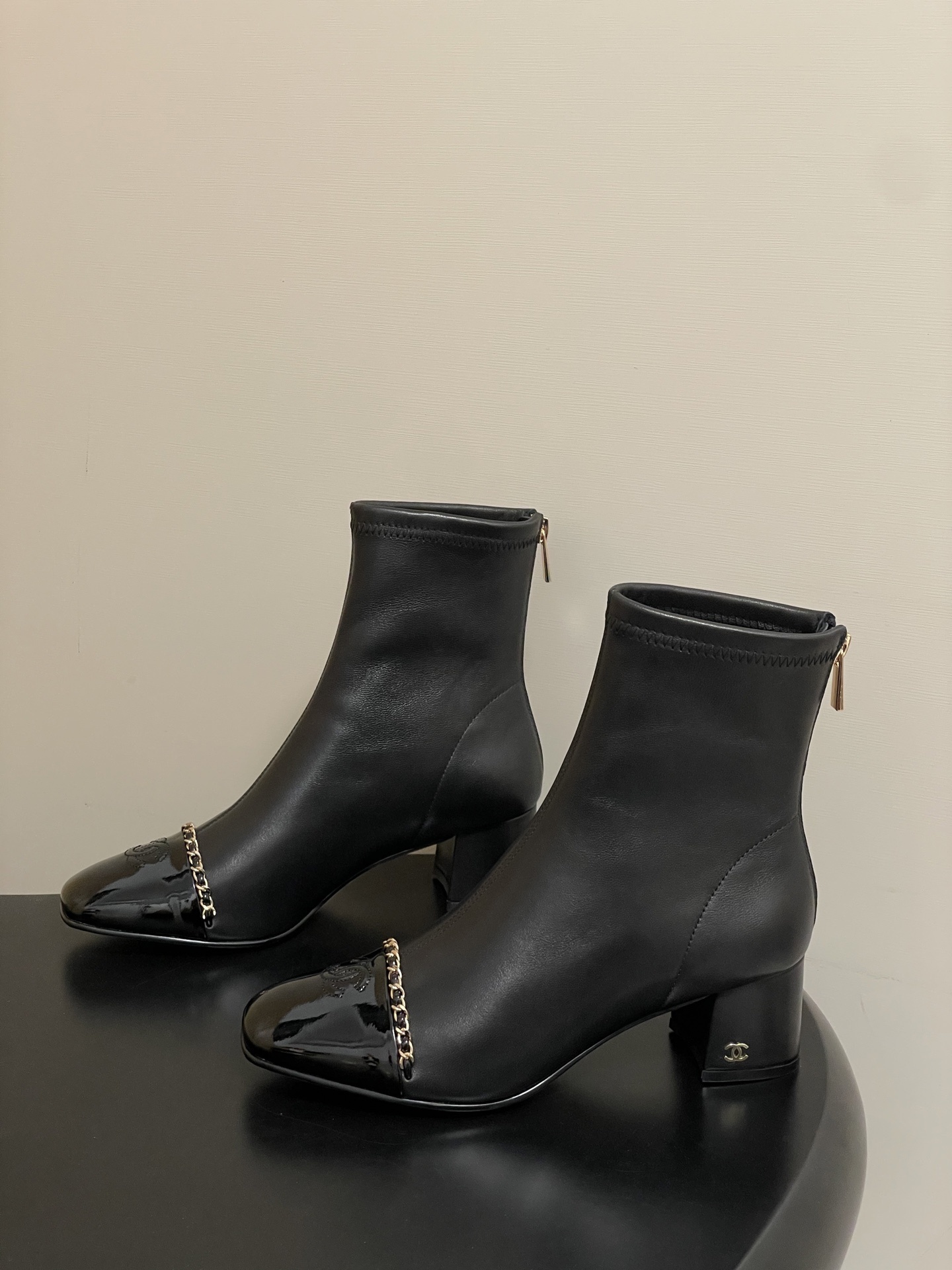 Elegant black leather ankle boots with gold chain detail and patent leather square toe cap on a black table. - Hình 3