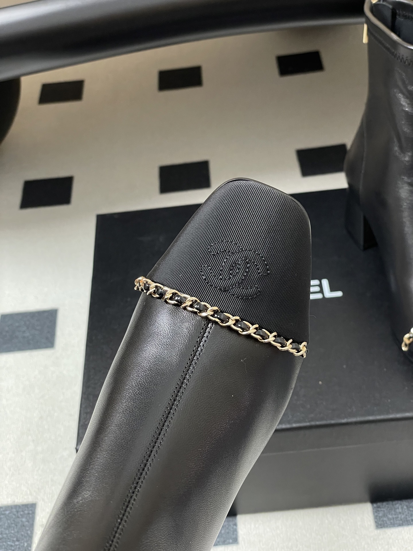 Pair of Chanel black leather ankle boots with gold chain detail and block heels on a black table - Hình 9