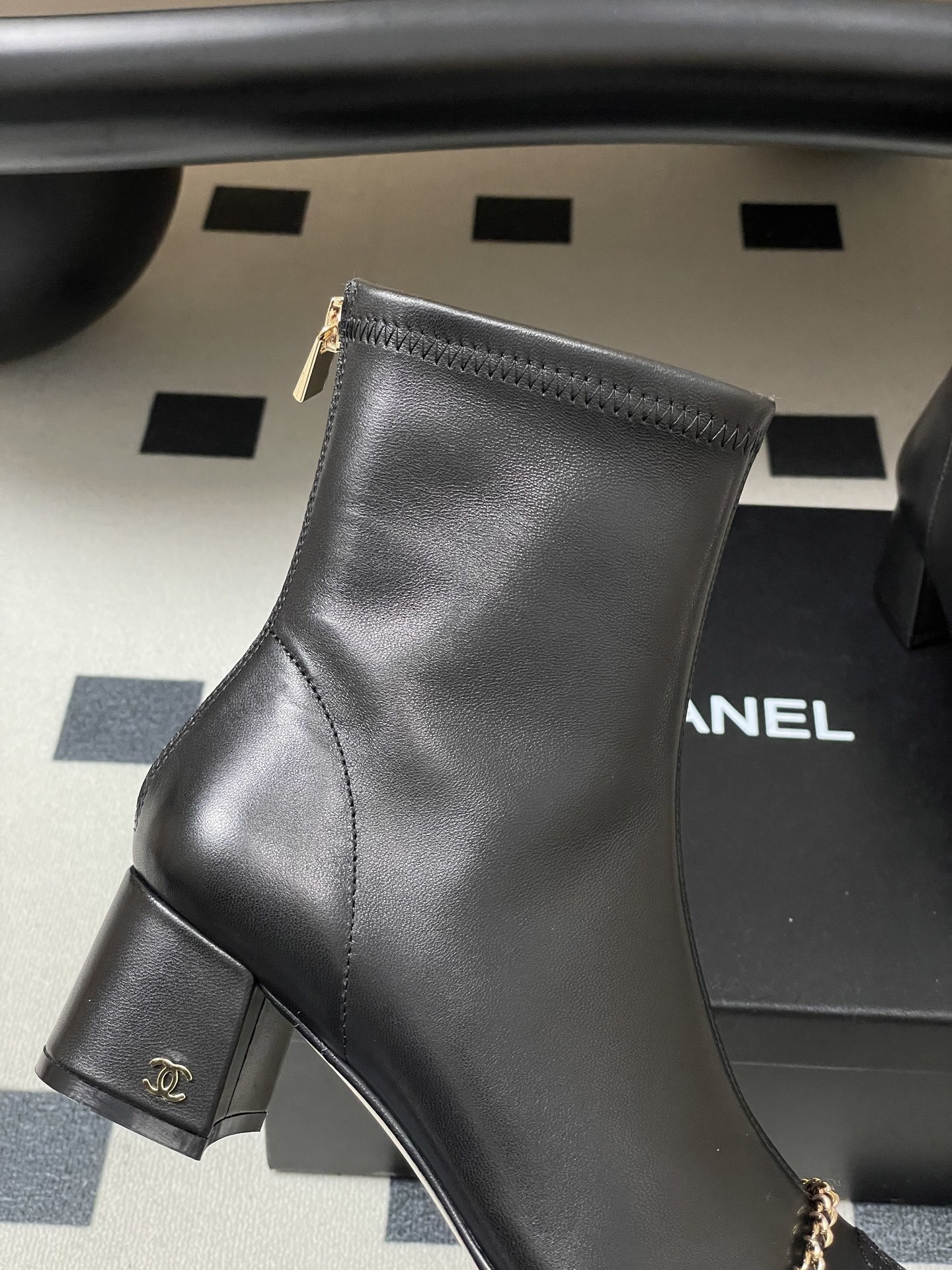 Pair of Chanel black leather ankle boots with gold chain detail and block heels on a black table - Hình 8
