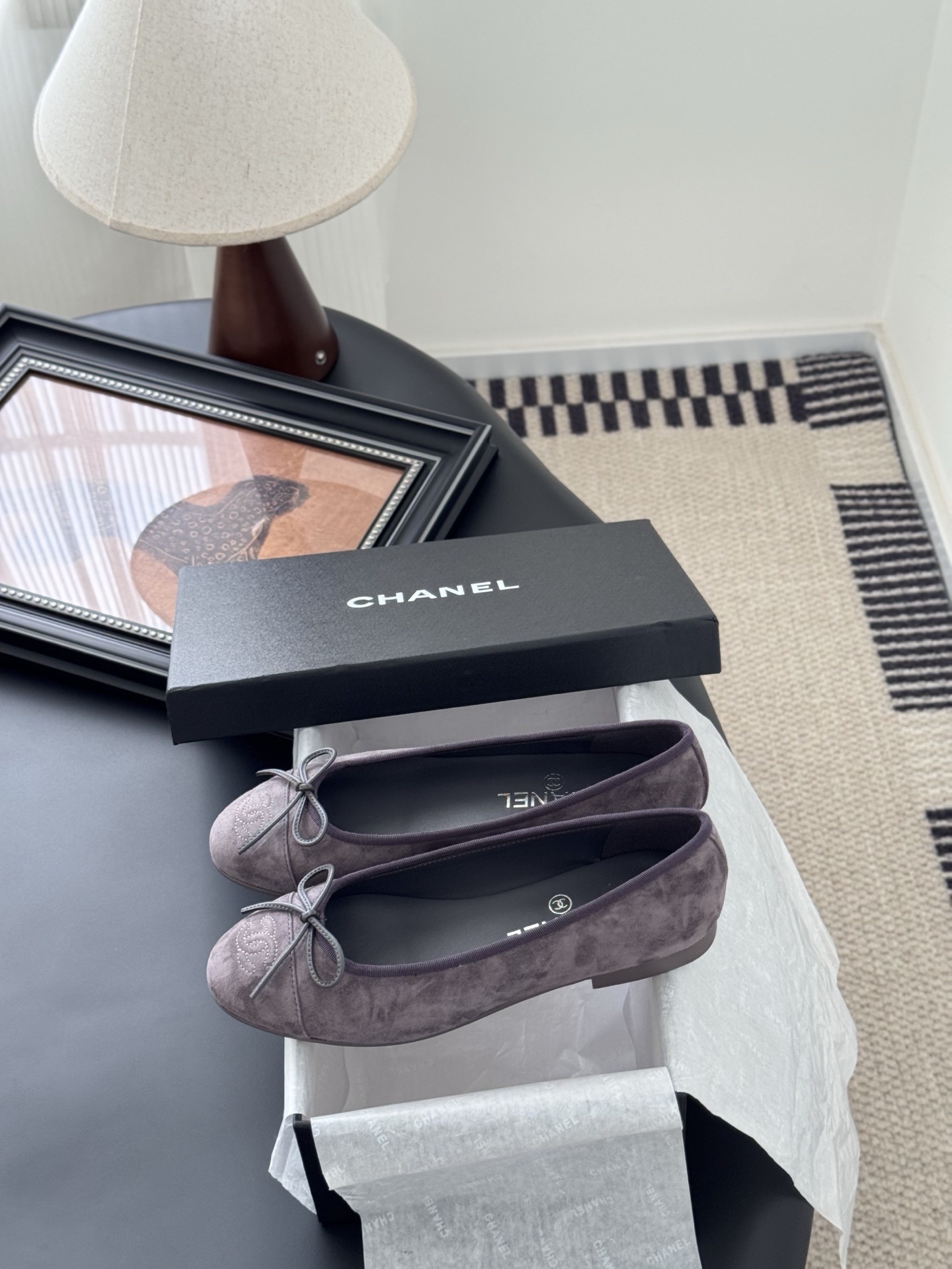 A pair of mauve suede Chanel ballerina flats featuring a bow and CC logo, displayed with a Chanel box. - Hình 9