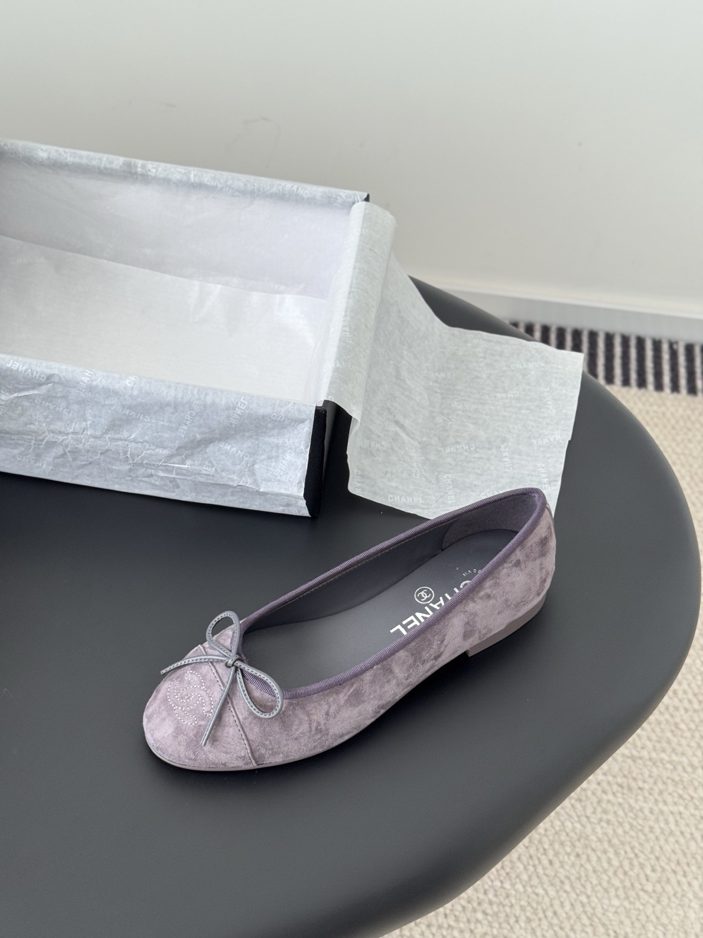 A pair of mauve suede Chanel ballerina flats featuring a bow and CC logo, displayed with a Chanel box. - Hình 5