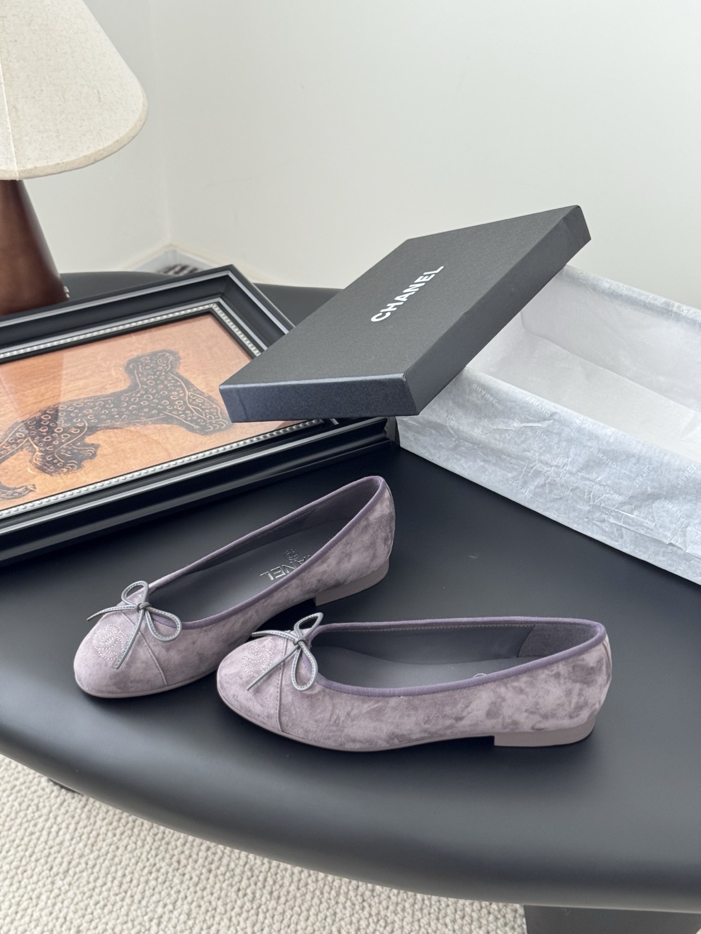 A pair of mauve suede Chanel ballerina flats featuring a bow and CC logo, displayed with a Chanel box. - Hình 2